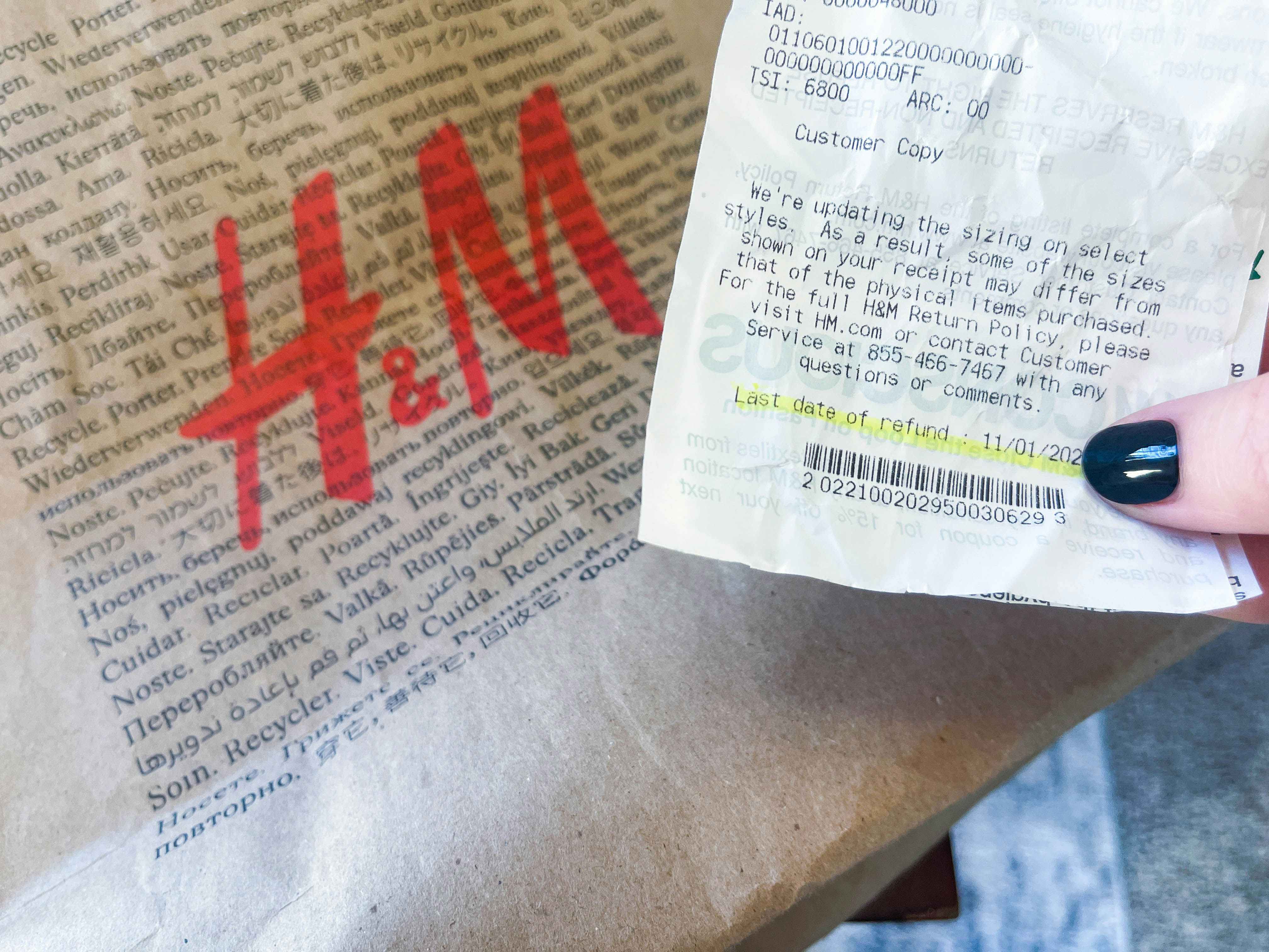 a person's hand holding a h & M receipt in front of a store bag 