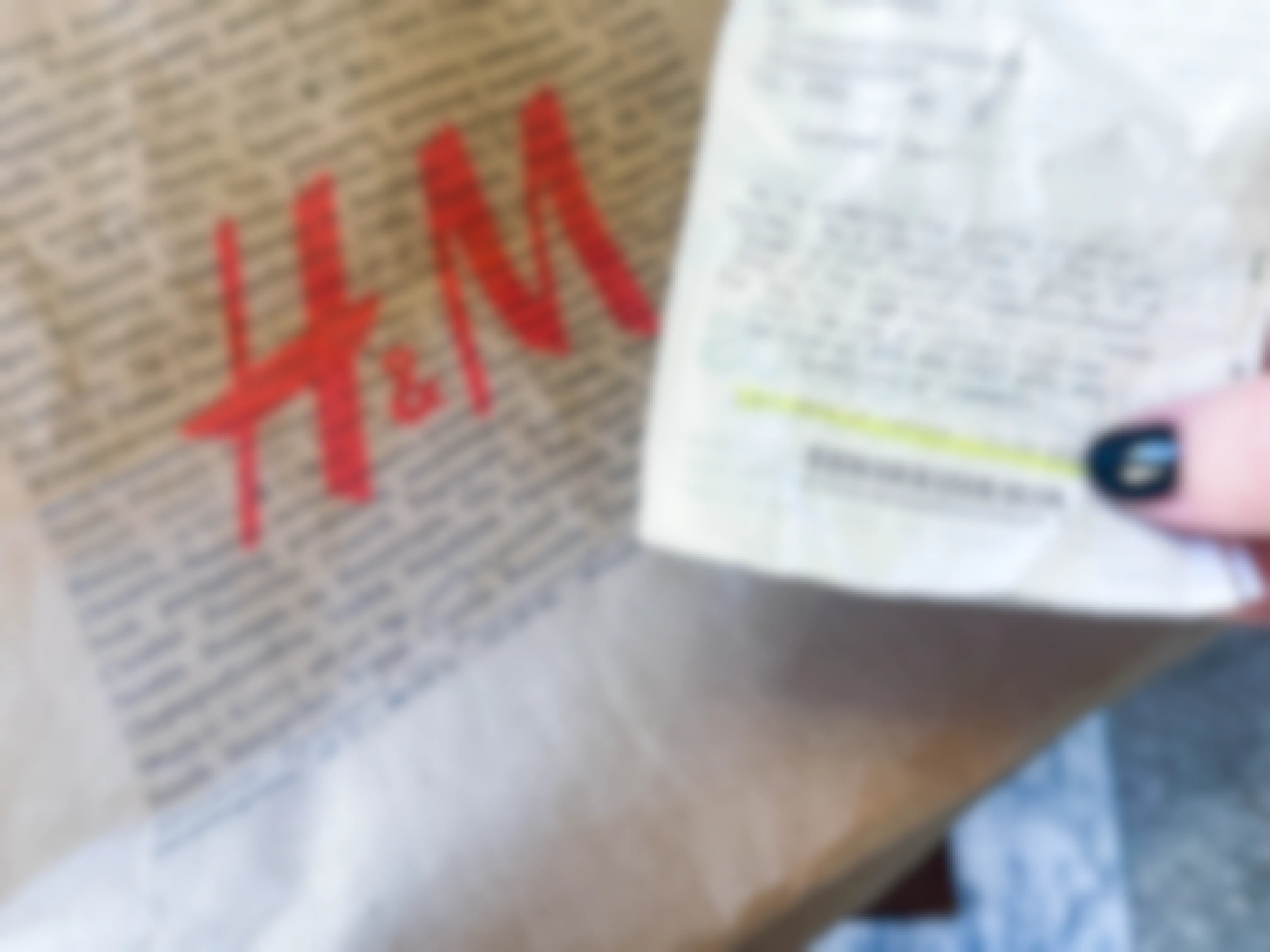 a person's hand holding a h & M receipt in front of a store bag 