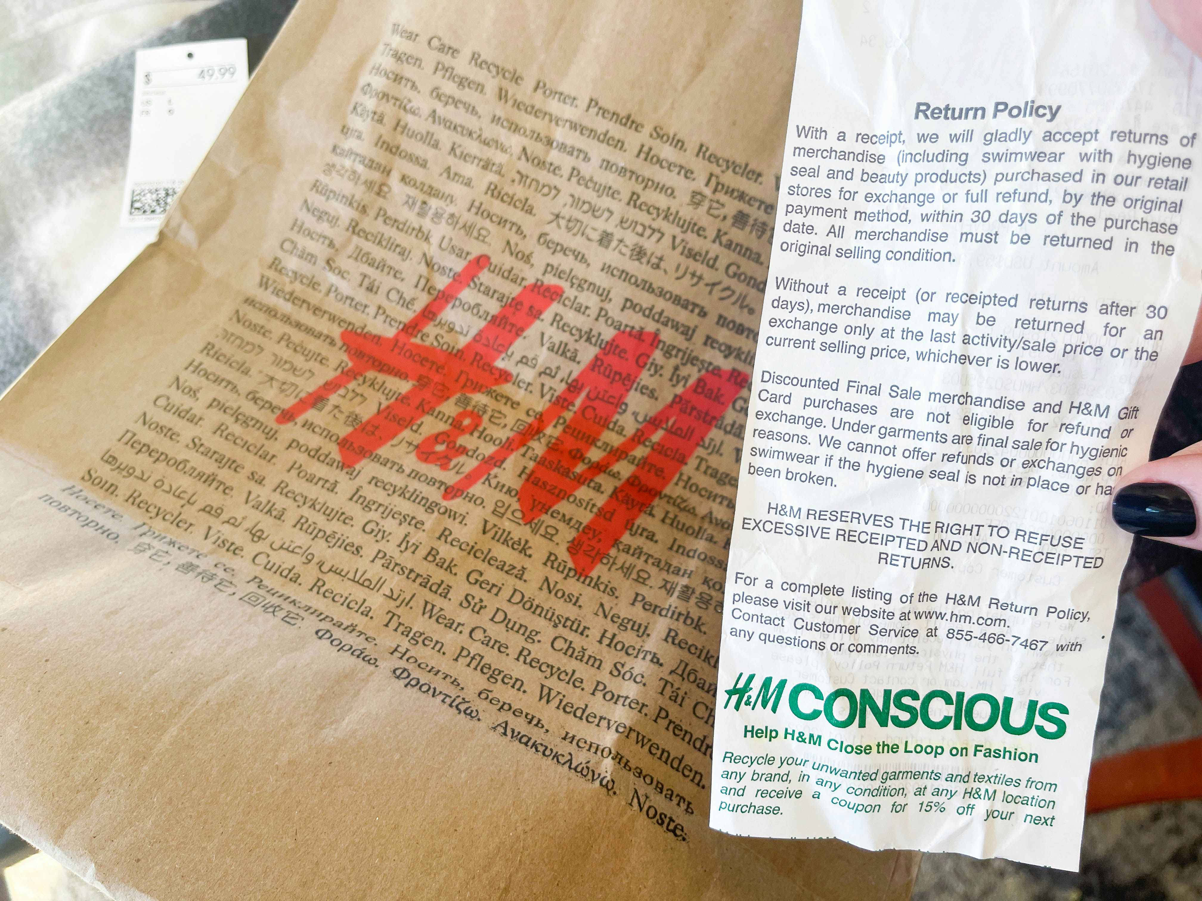 a person's hand holding a h & M receipt in front of a store bag