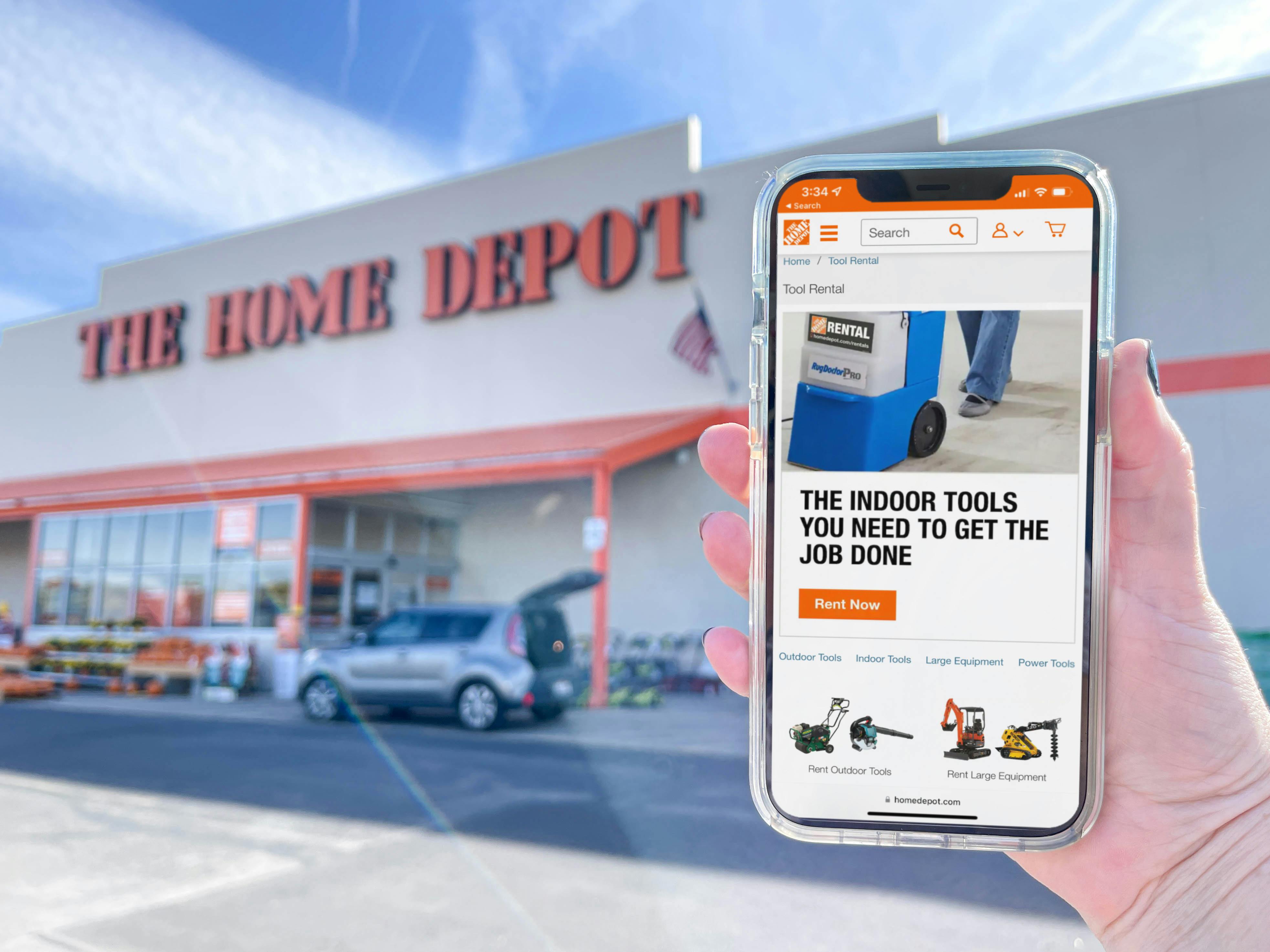 A person's hands holding a cellphone with home depot tool rentals in front of home depot store 