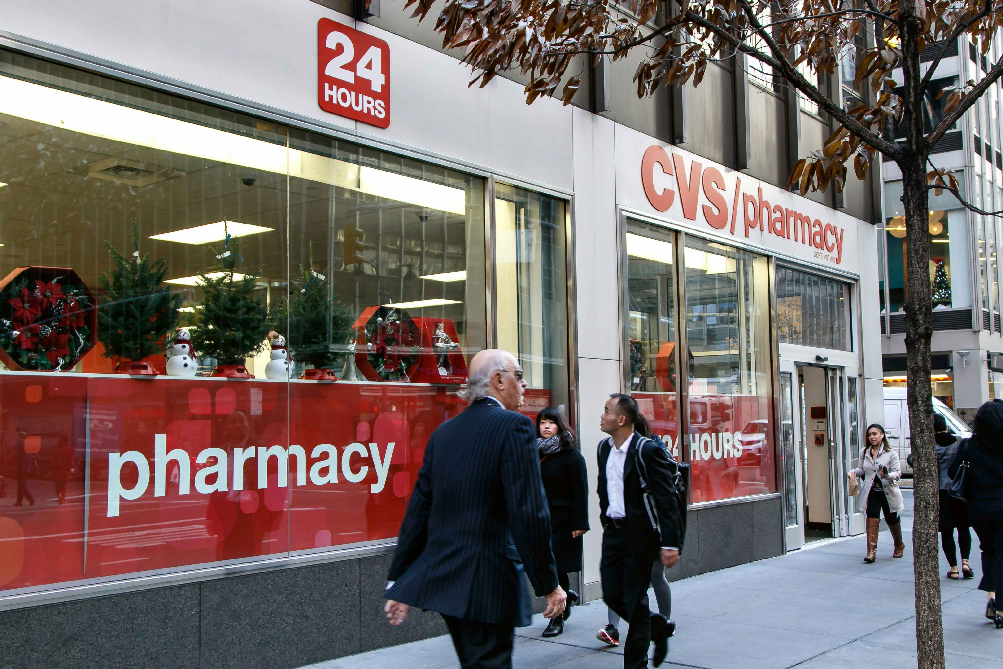 People walking by a CVS with miniature Christmas trees on display in the windows.