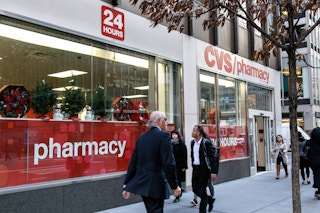 People walking by a CVS with miniature Christmas trees on display in the windows.