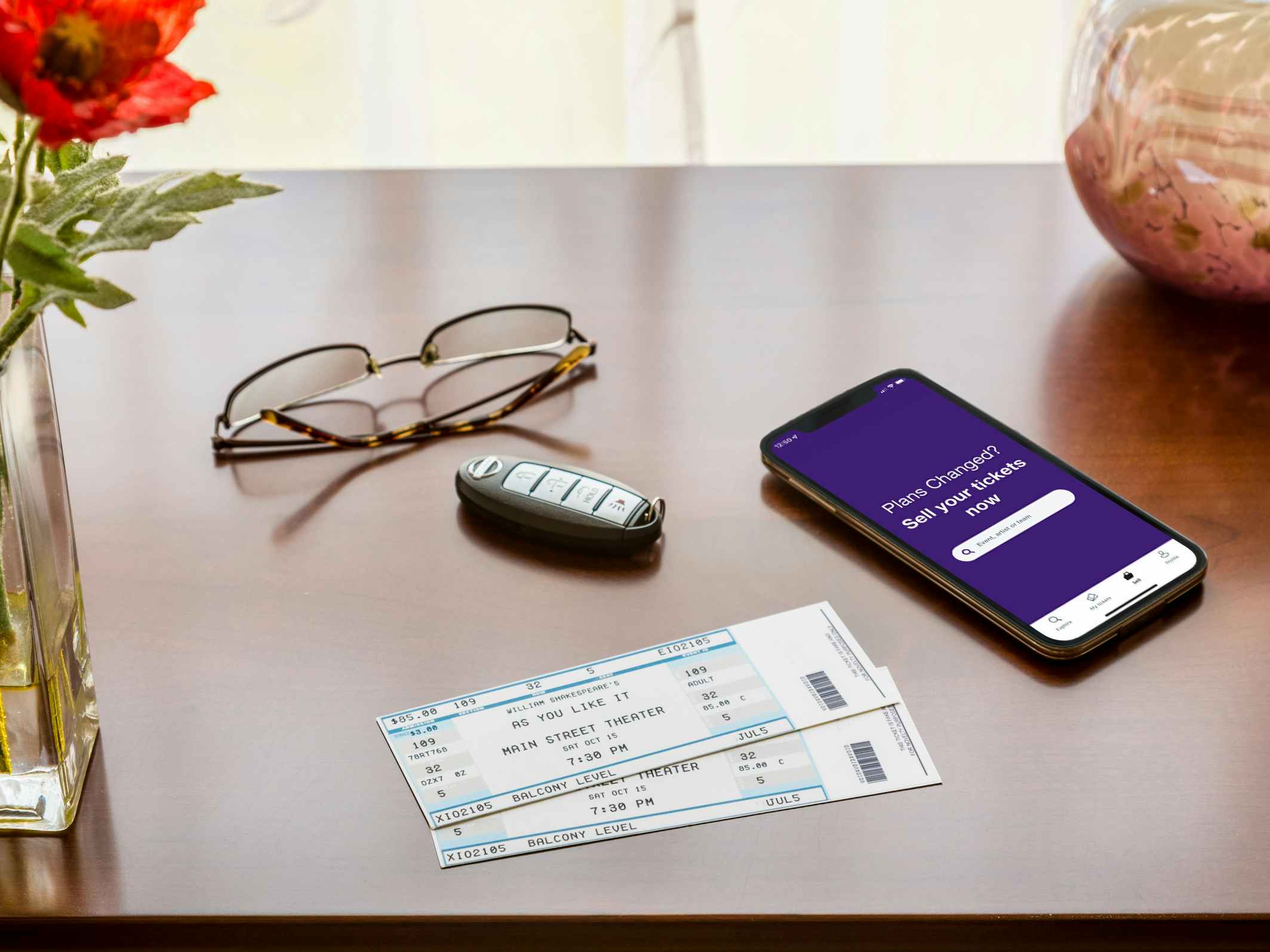 Some tickets on a table next to a phone displaying the StubHub selling page in their mobile app