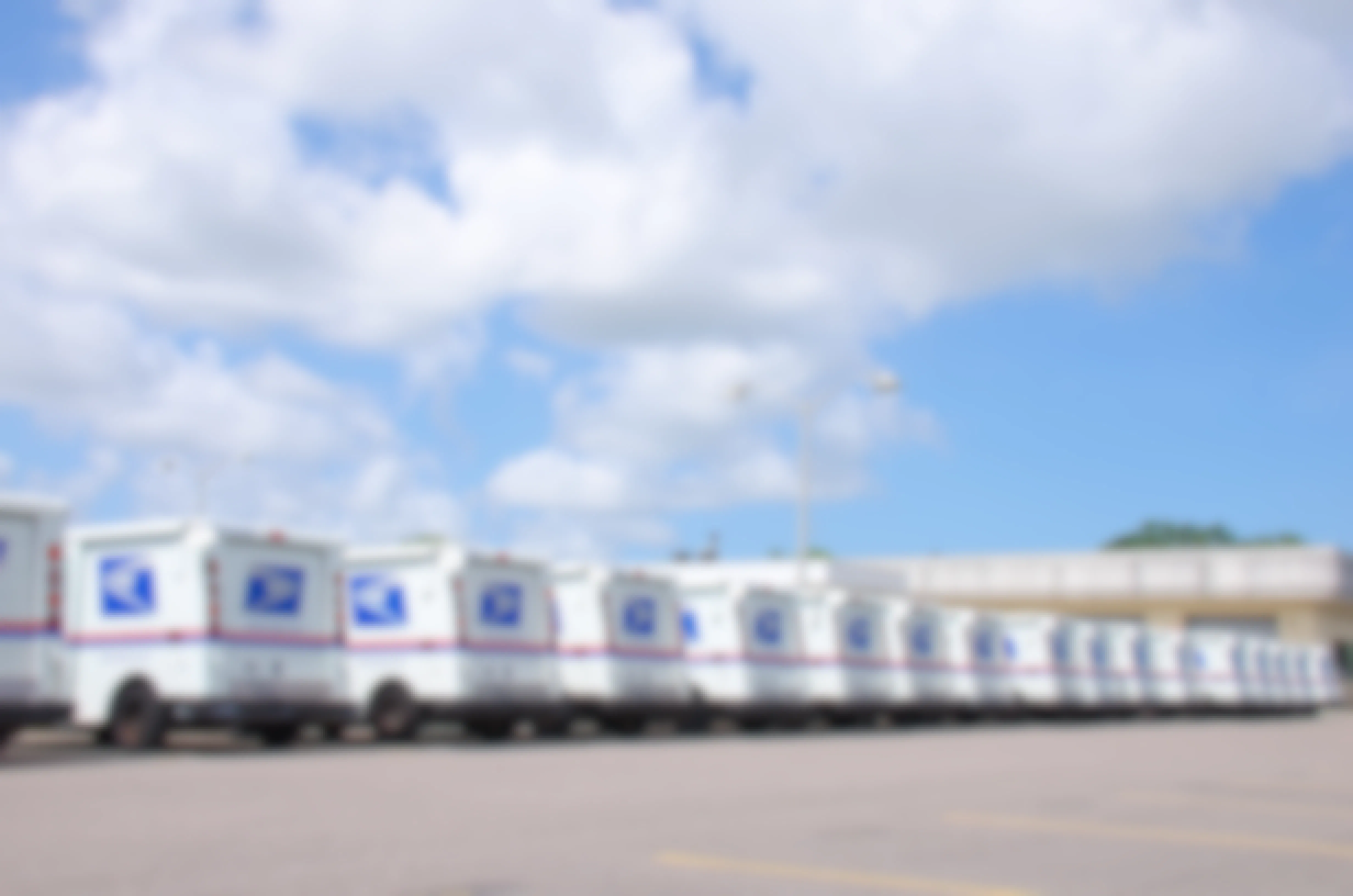 A row of U.S. Postal Service mail trucks in a parking lot.