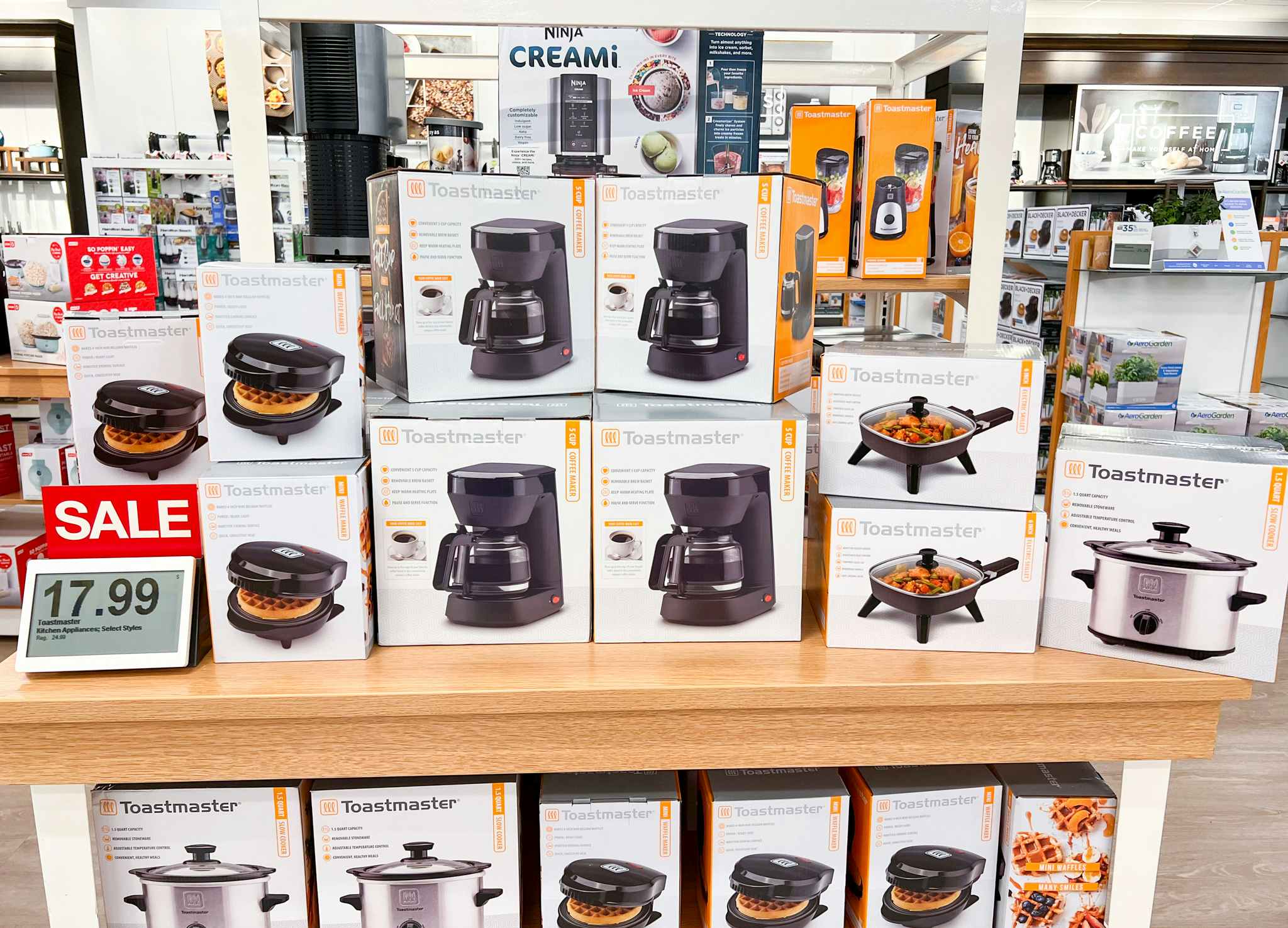 Table of waffle makers, coffee makers and skillets next to a sale sign