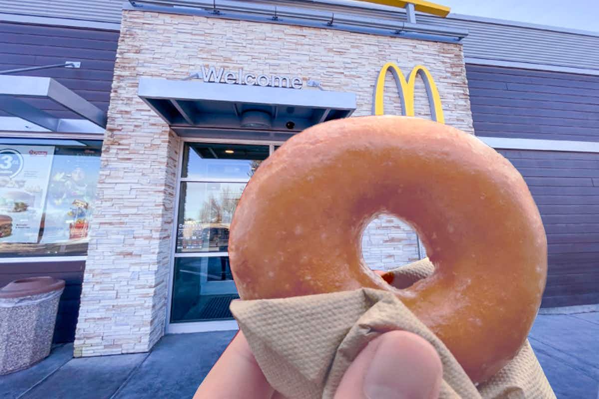 someone holding a Krispy Kreme doughnut in front of a McDonald's entrance.