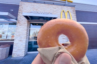 someone holding a Krispy Kreme doughnut in front of a McDonald's entrance.