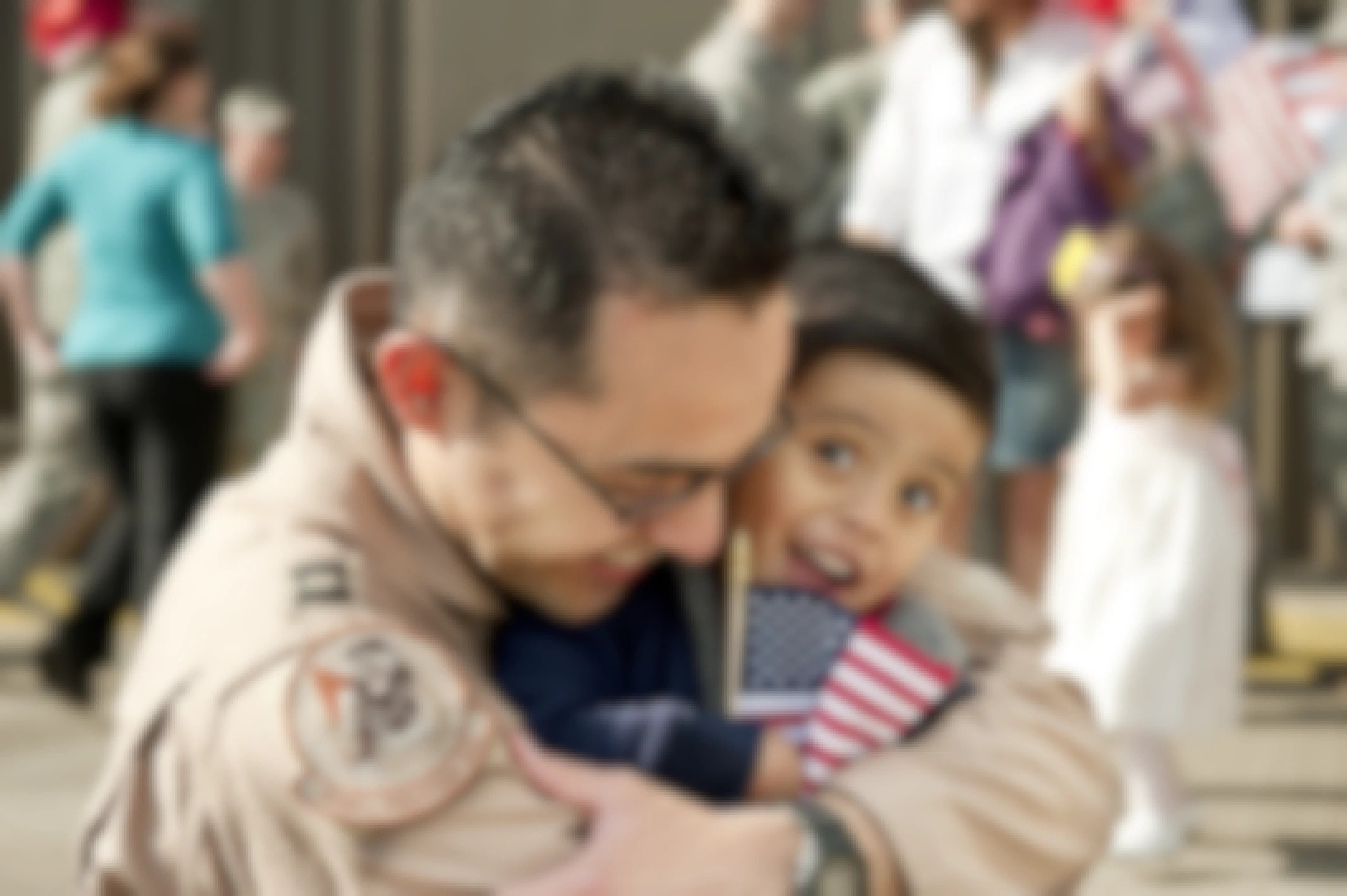 A military dad hugging his kid holding an American flag