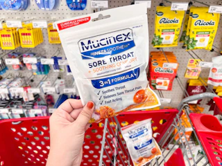 hand holding mucinex cough drops above target cart