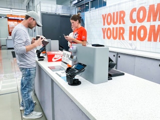 A person standing at the checkout desk in a Nike store, looking at some shoes the cashier is ringing up.