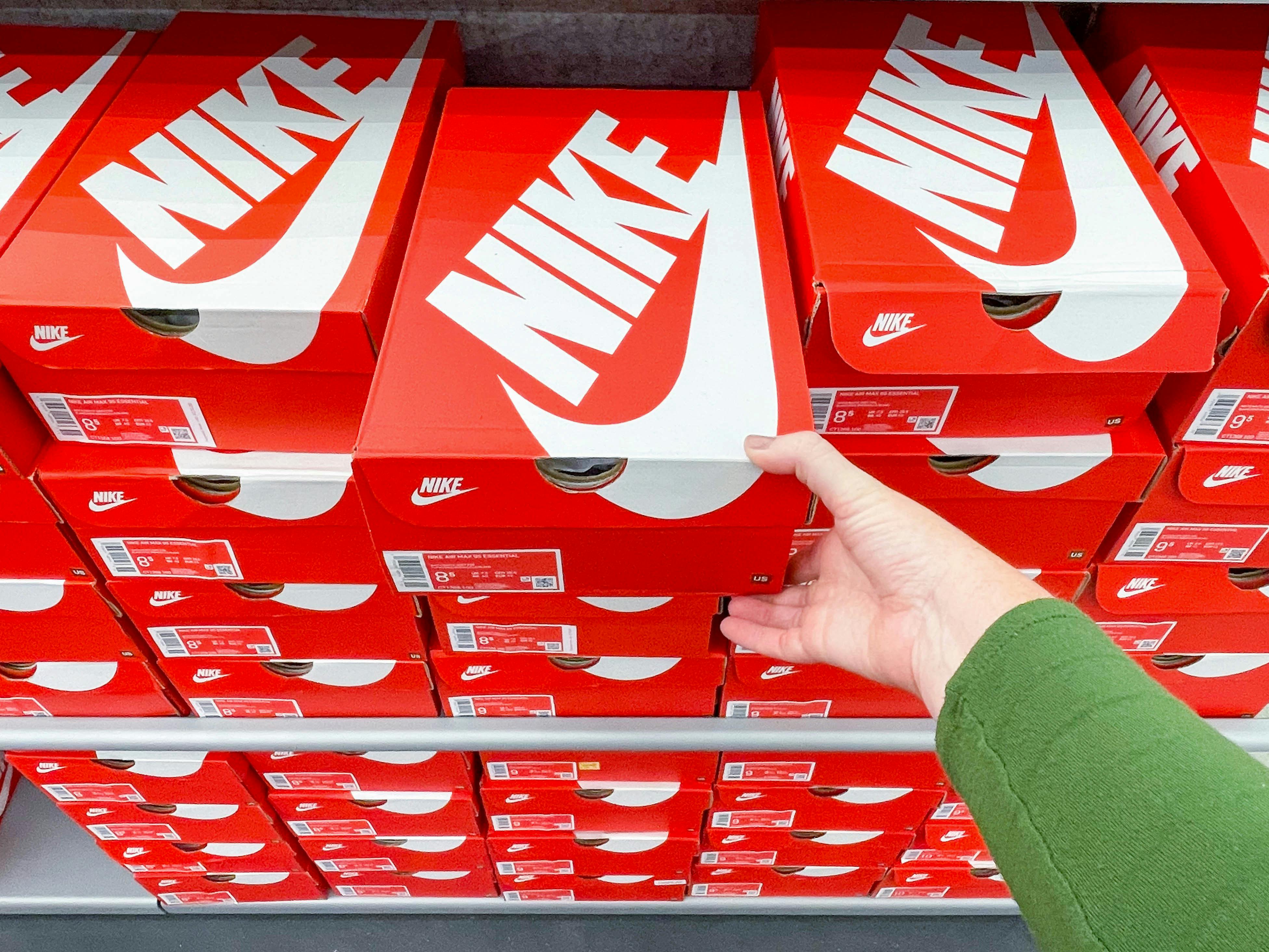 A person's hand taking a box of Nike shoes from a shelf.