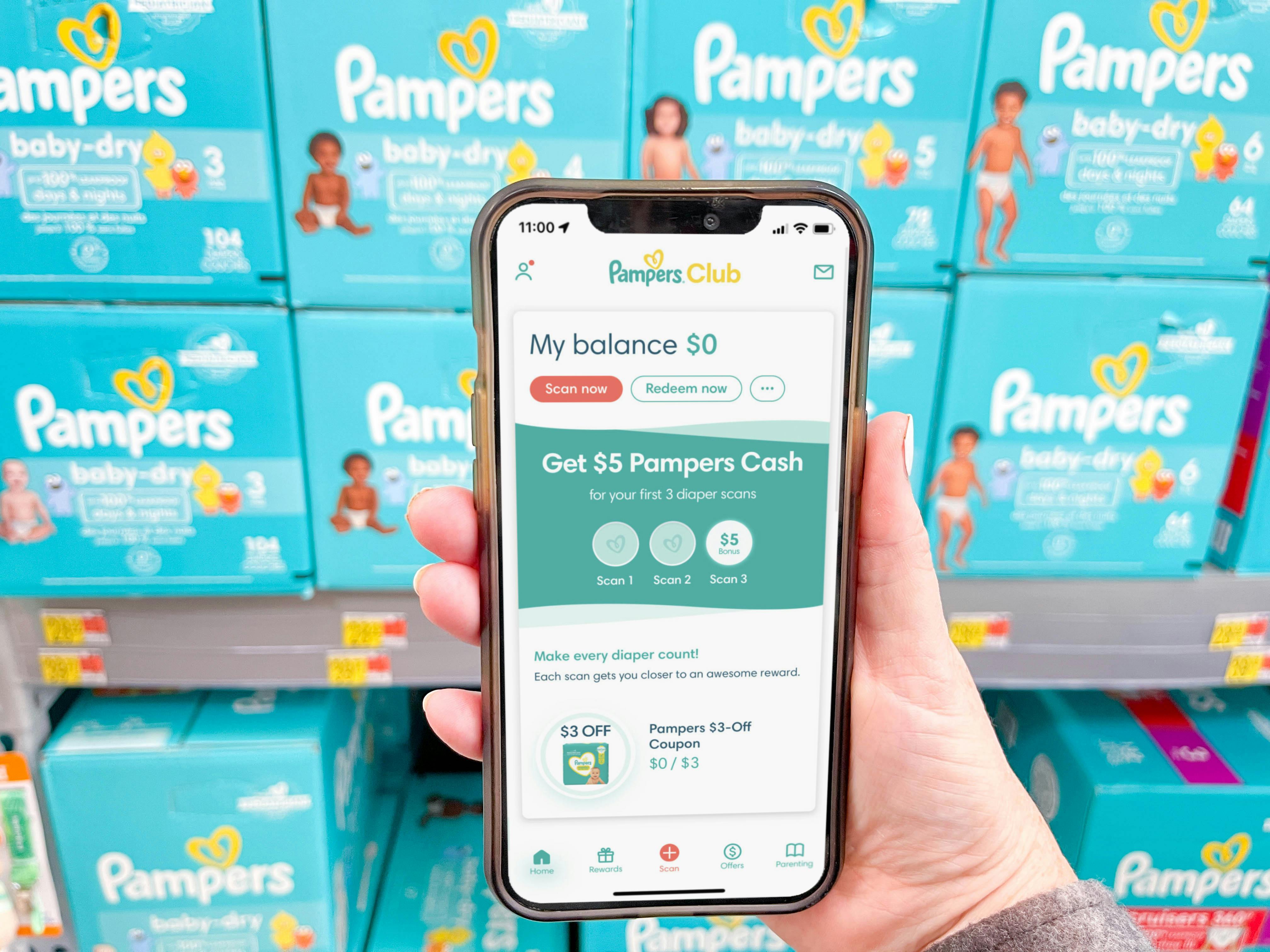 a hand holding a cellphone with pampers rewards app on screen in front of pampers boxes 