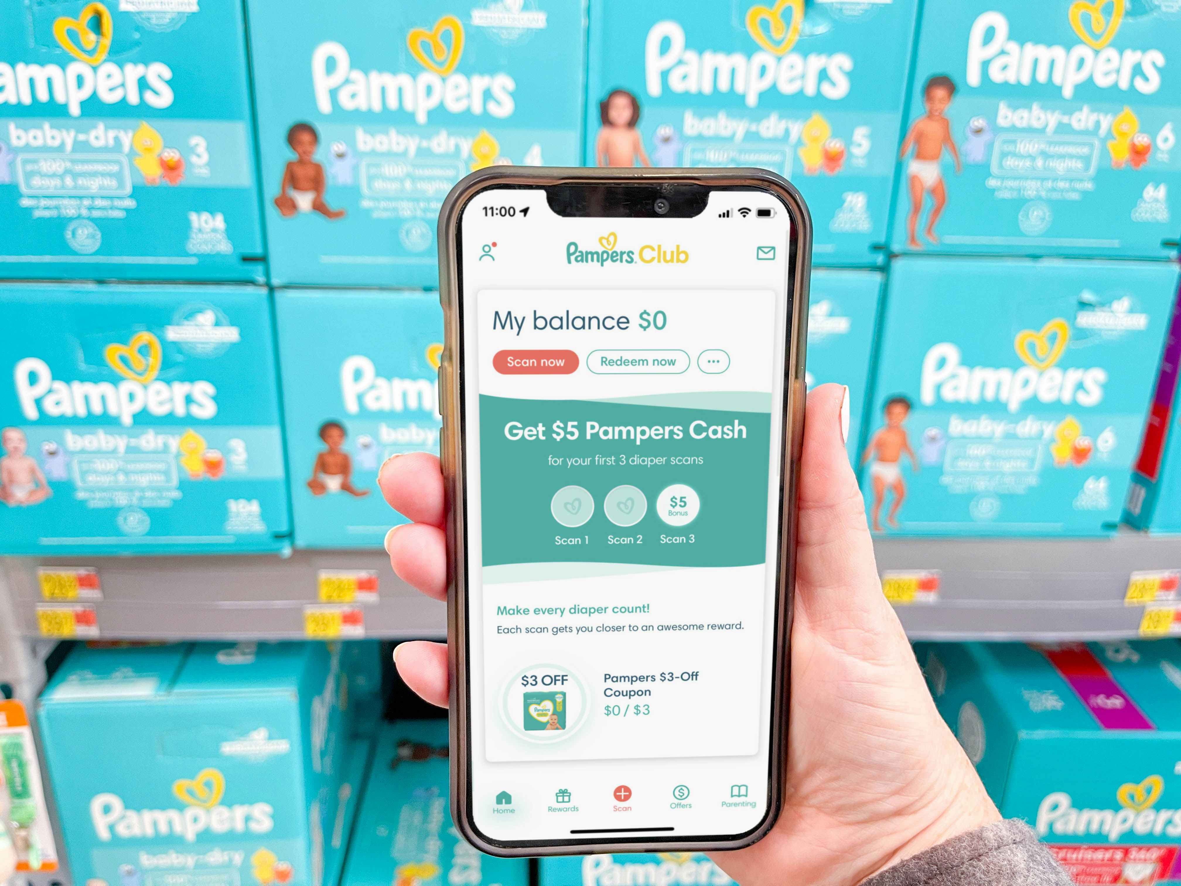 a hand holding a cellphone with pampers rewards app on screen in front of pampers boxes 