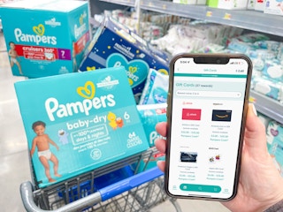 a hand holding a cellphone with pampers rewards app on screen in front of pampers boxes