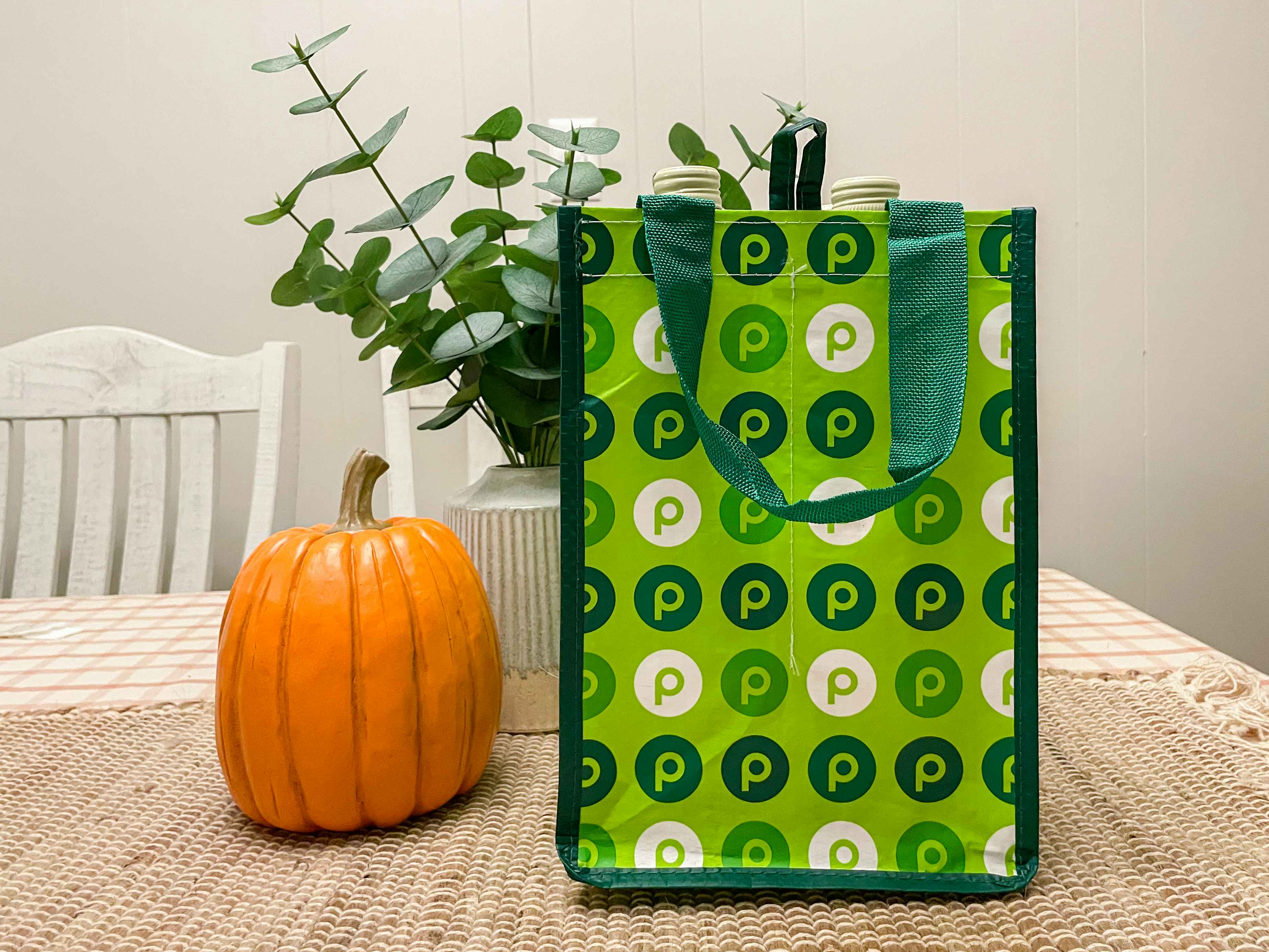 A Publix reusable wine bag on a table next to a pumpkin