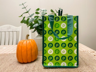A Publix reusable wine bag on a table next to a pumpkin