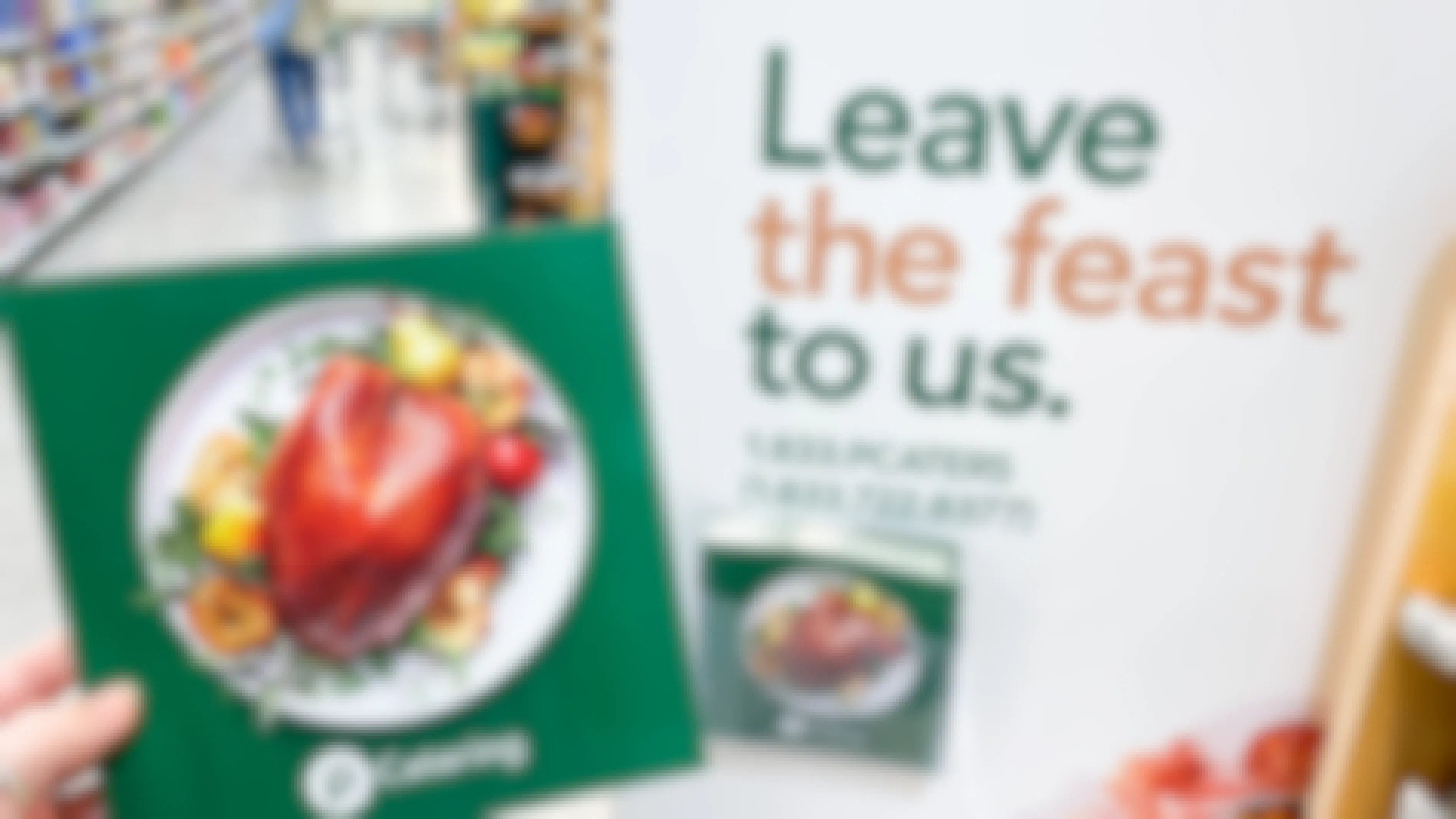 A person's hand holding up a Thanksgiving booklet next to a sign in Publix that says "Leave the Feast to us