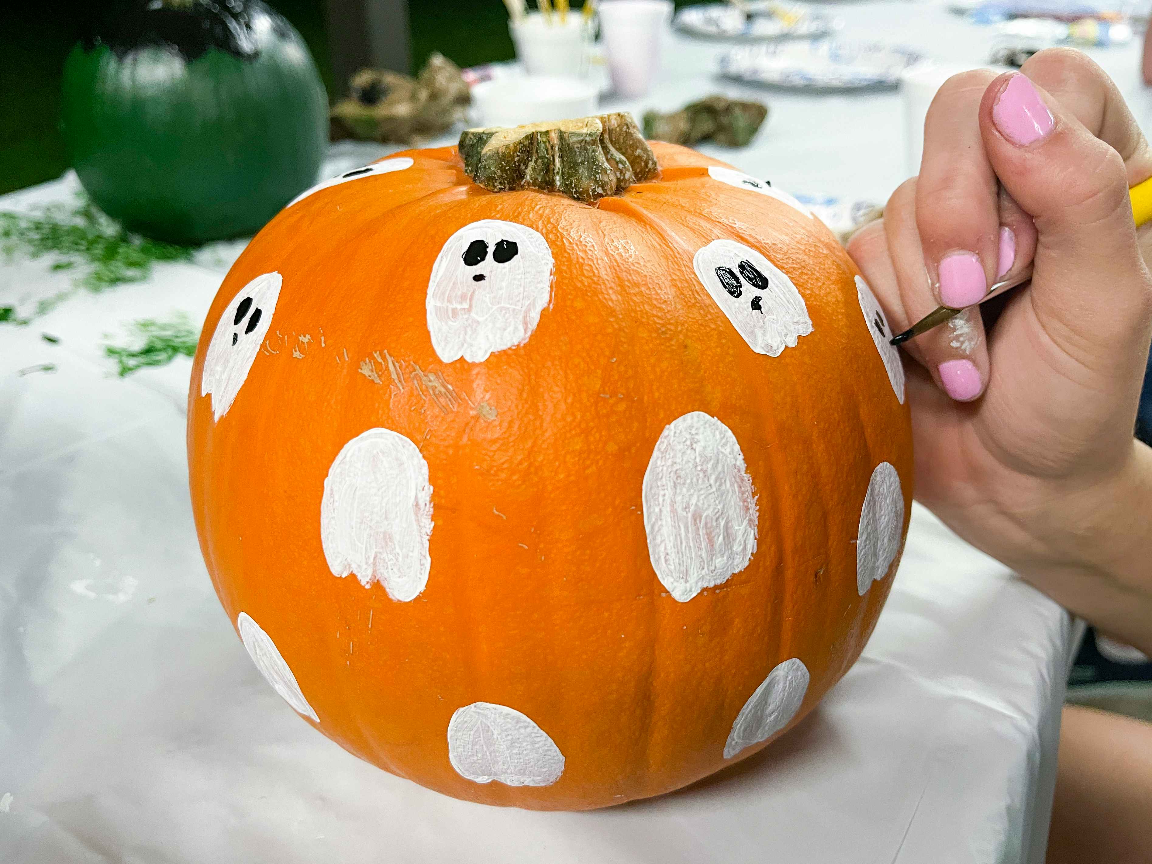 A person painting small ghosts onto a pumpkin.