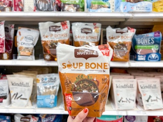 hand holding rachael ray dog treats in front of shelf