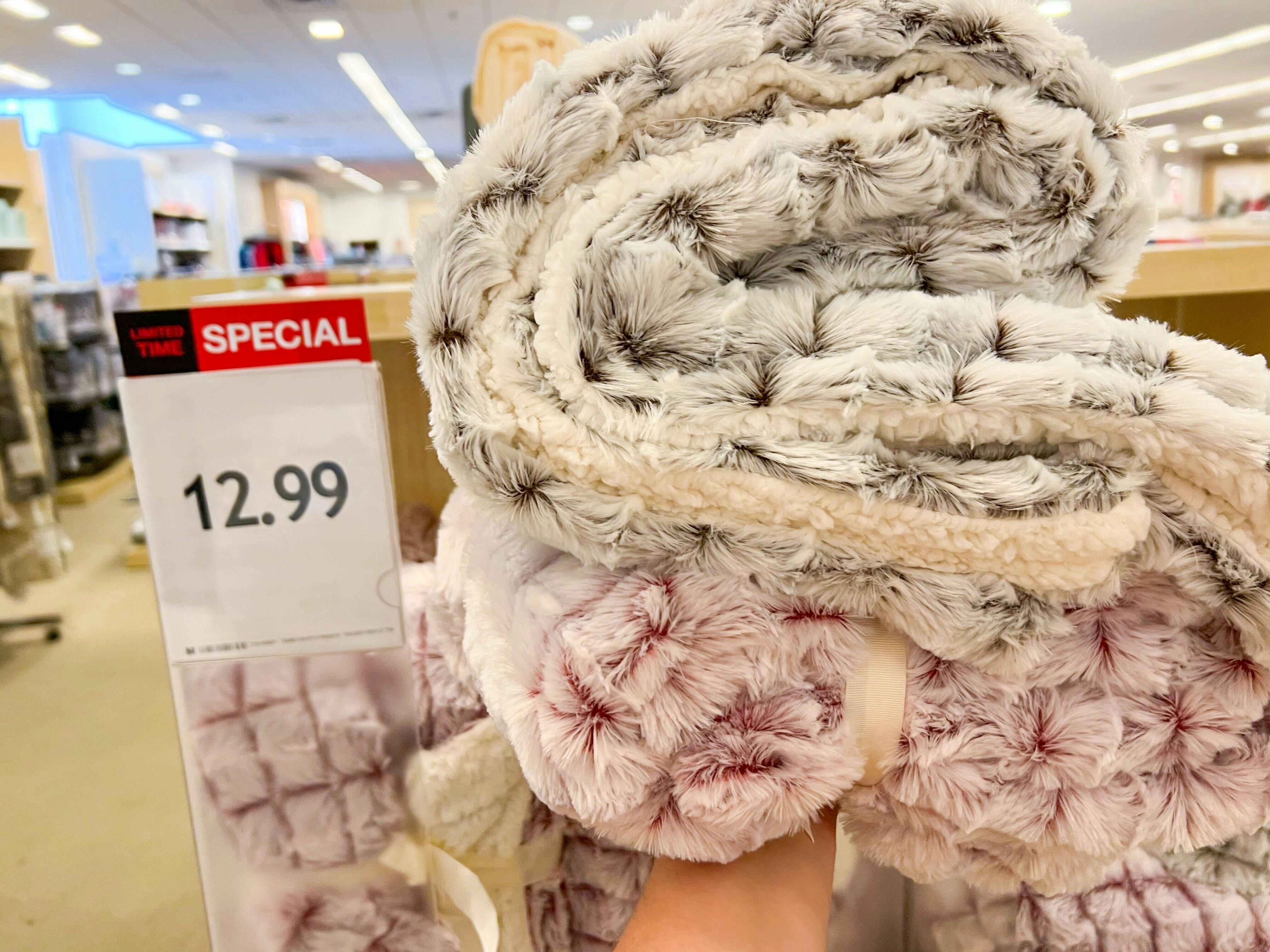 someone holding a sherpa and mink blanket by a sale sign