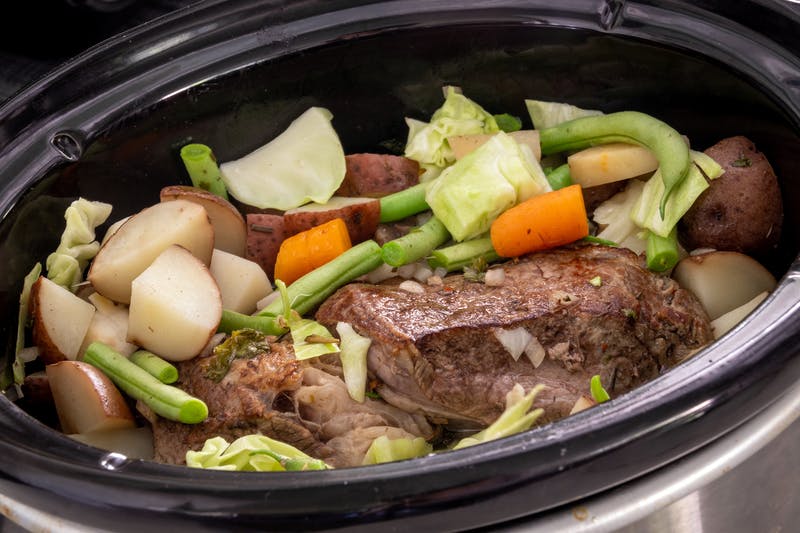 a slow cooker with a roast and vegetables.
