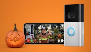 A Ring video doorbell camera next to a phone displaying a video feed and a pumpkin on an orange background
