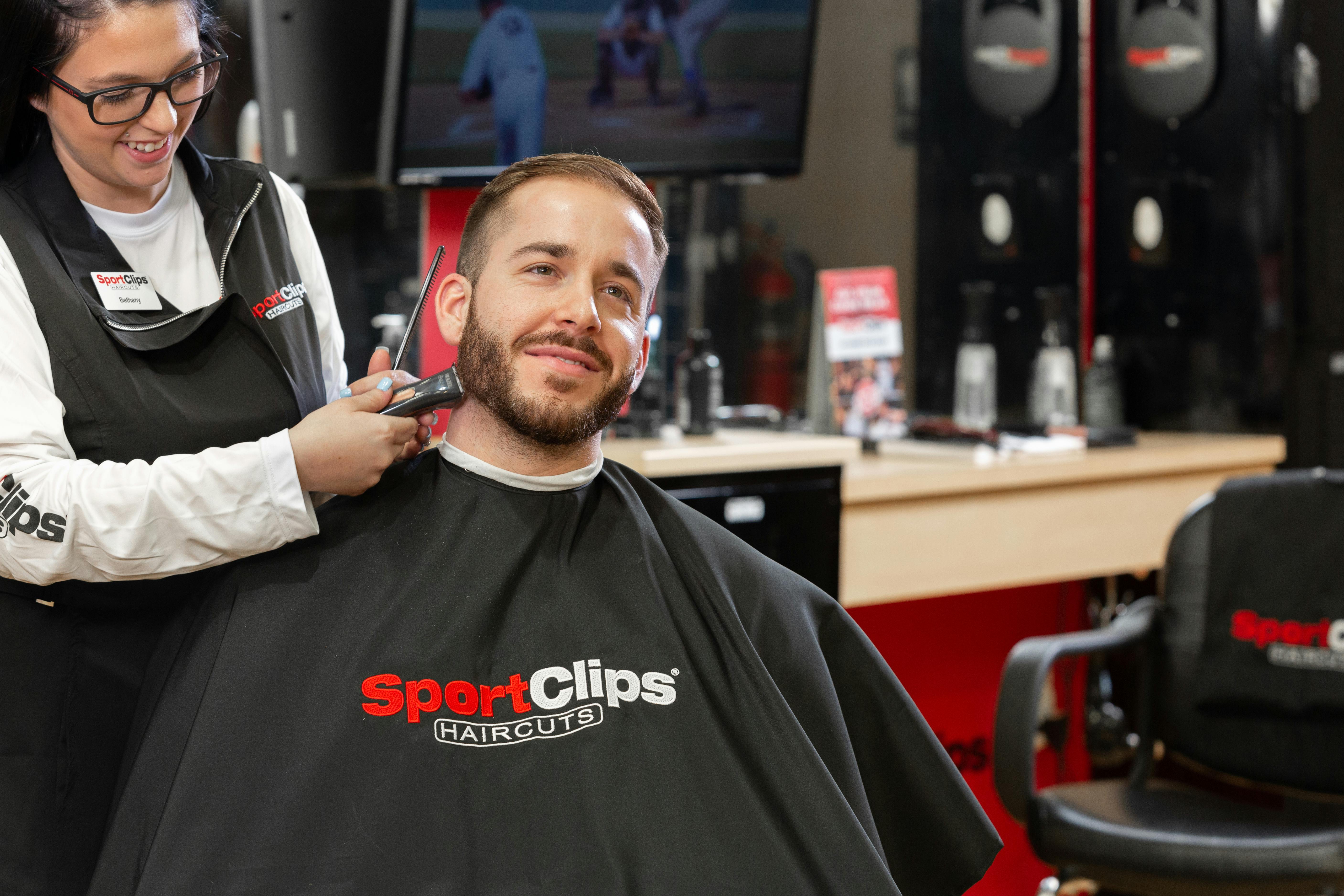 A stylist trimming a mans beard at Sport Clips