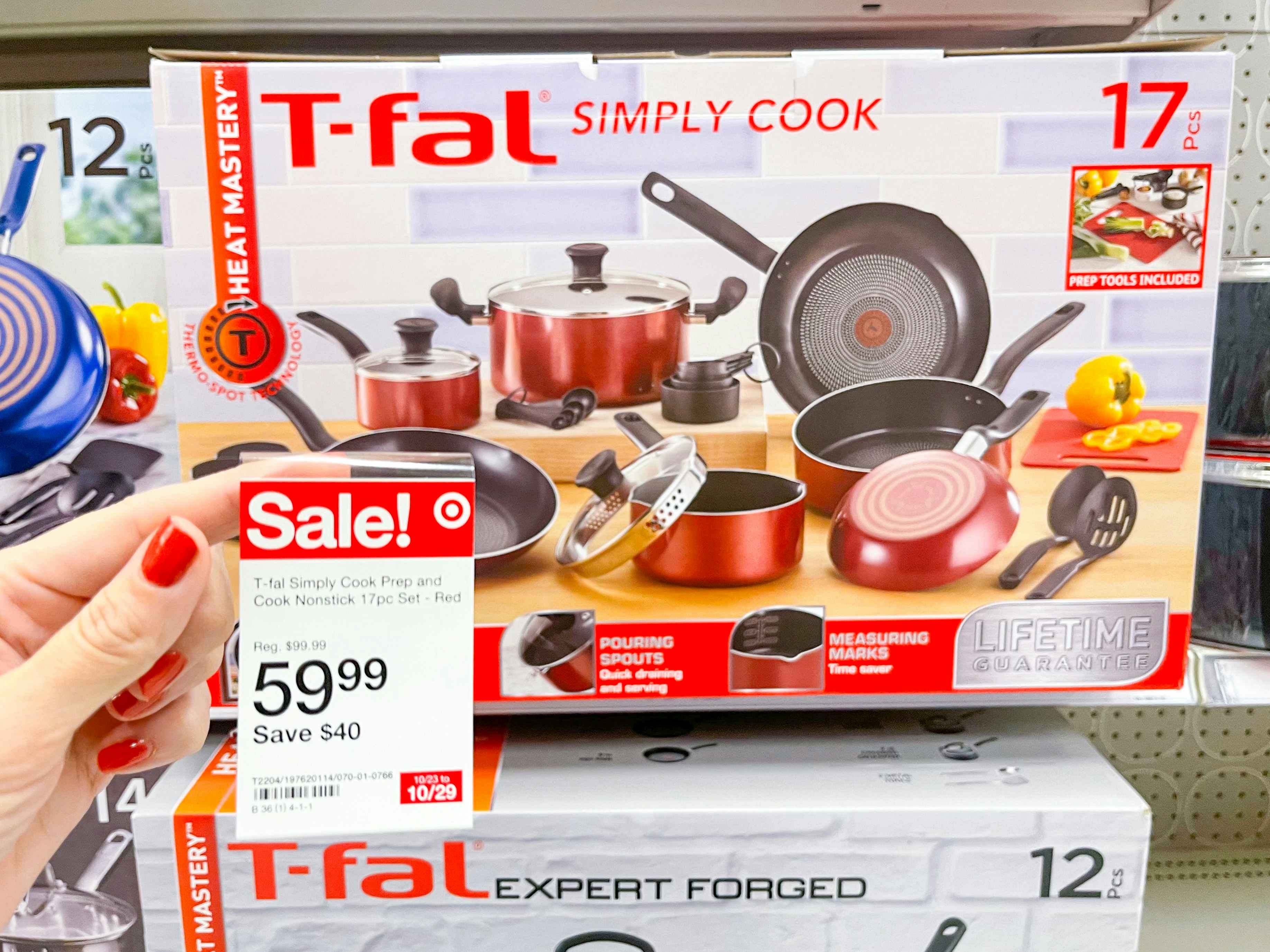 A box of T-fal simply cook cookware sitting on a store shelf with a sale sticker held out in front of it by hand.