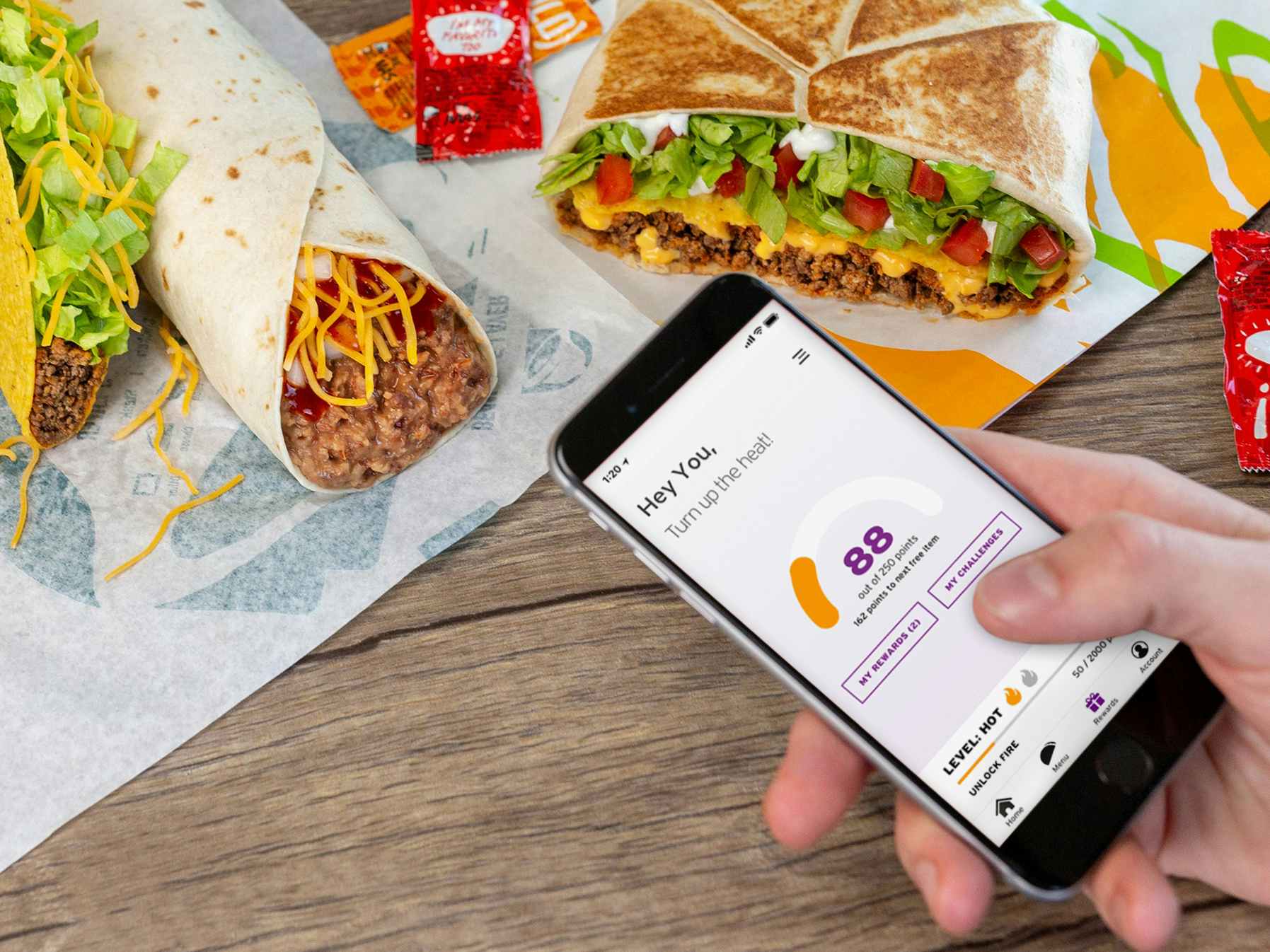 person holding phone with taco bell rewards and food on table