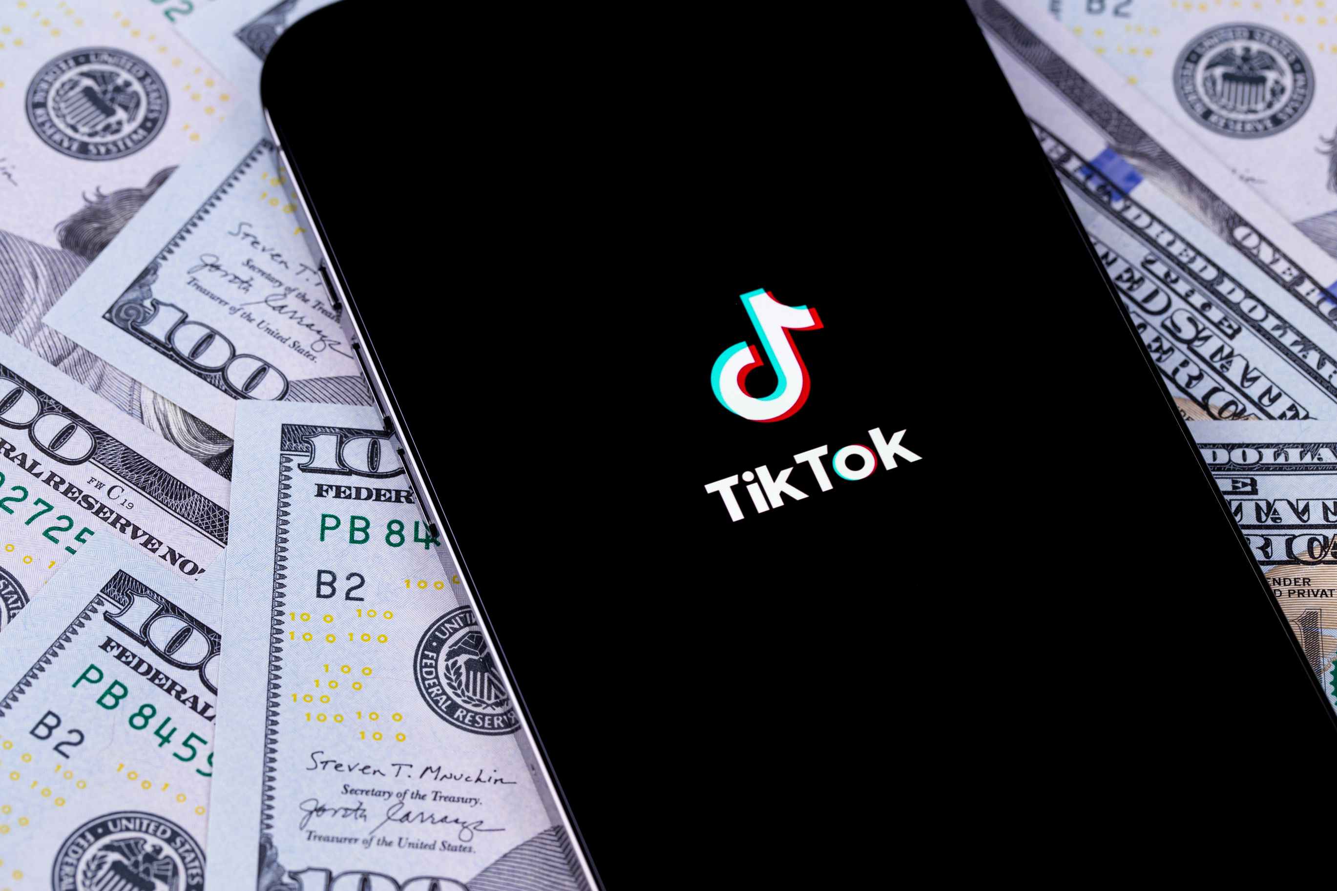 A phone displaying the TikTok app laying on a pile of cash.