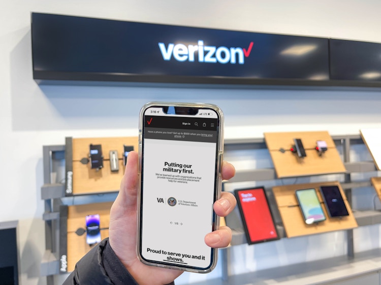 a hand holding a cellphone with military page on app in front of verizon sign 