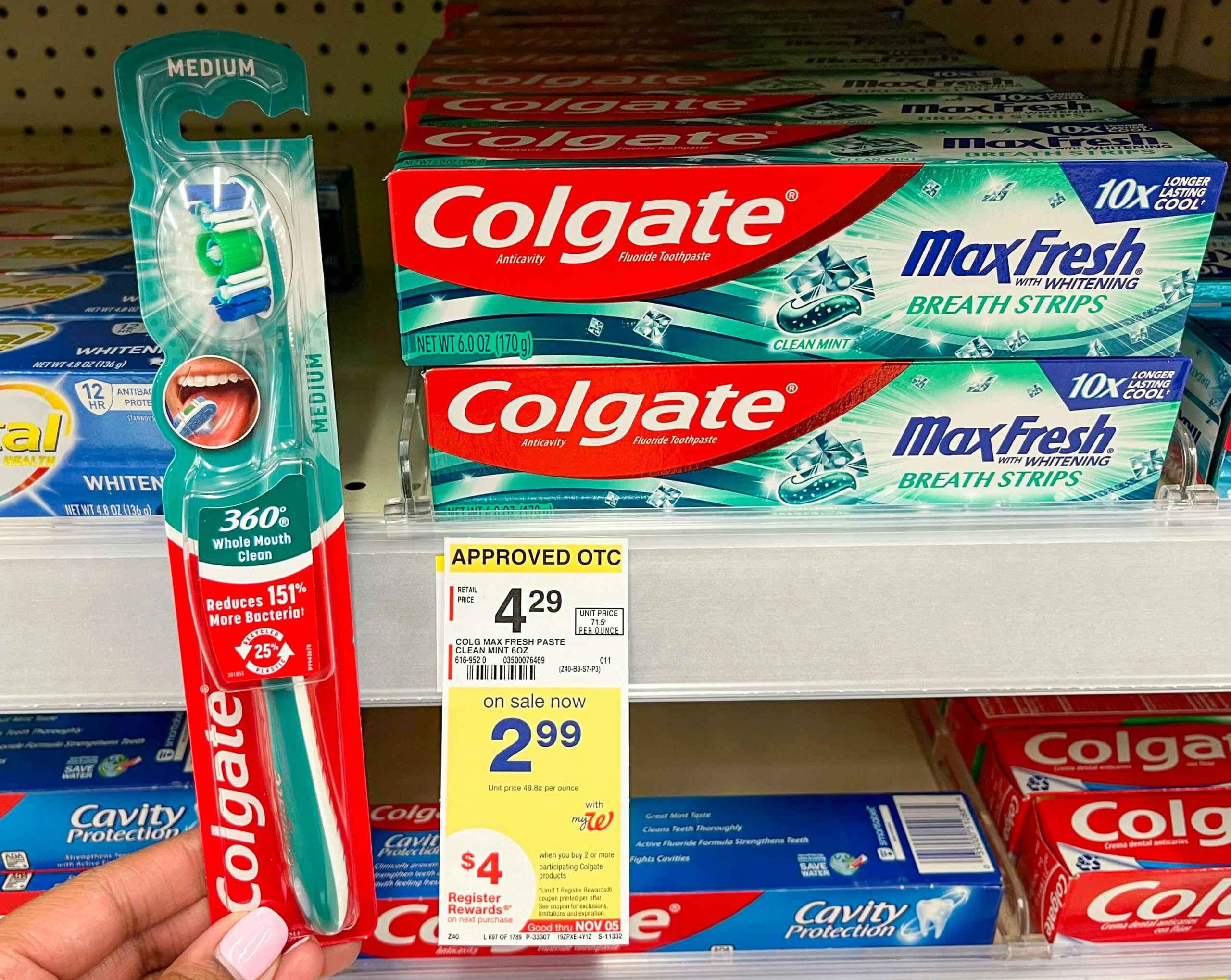 hand holding Colgate manual toothbrush next to Colgate toothpaste and sales tag on shelf