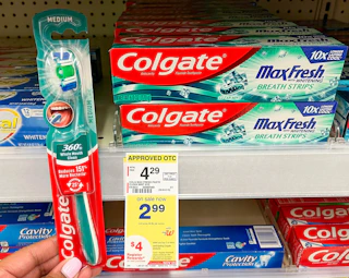 hand holding Colgate manual toothbrush next to Colgate toothpaste and sales tag on shelf