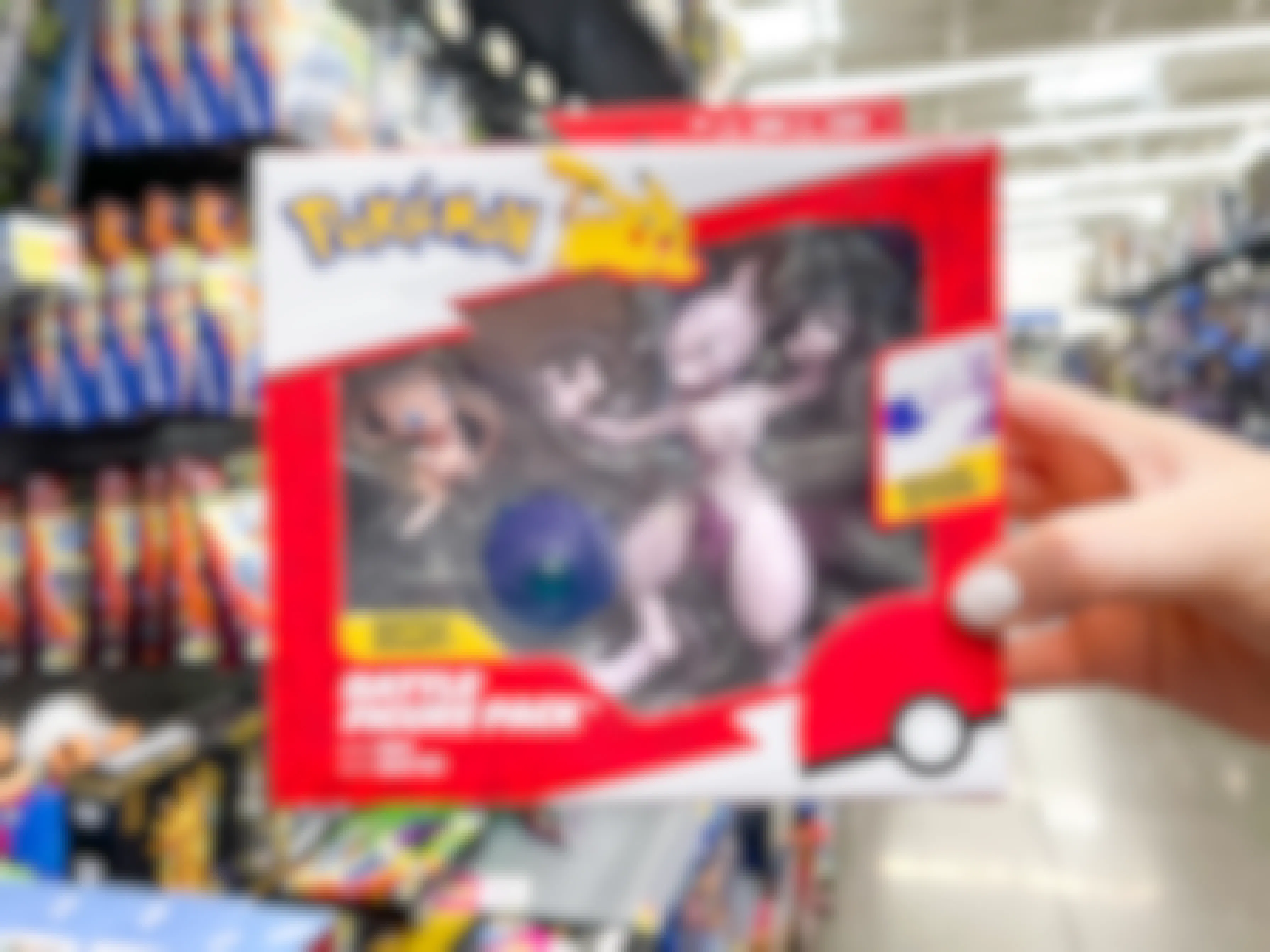 A person's hand holding a Pokemon Mew and Mewtwo figure pack in front of a Walmart shelf