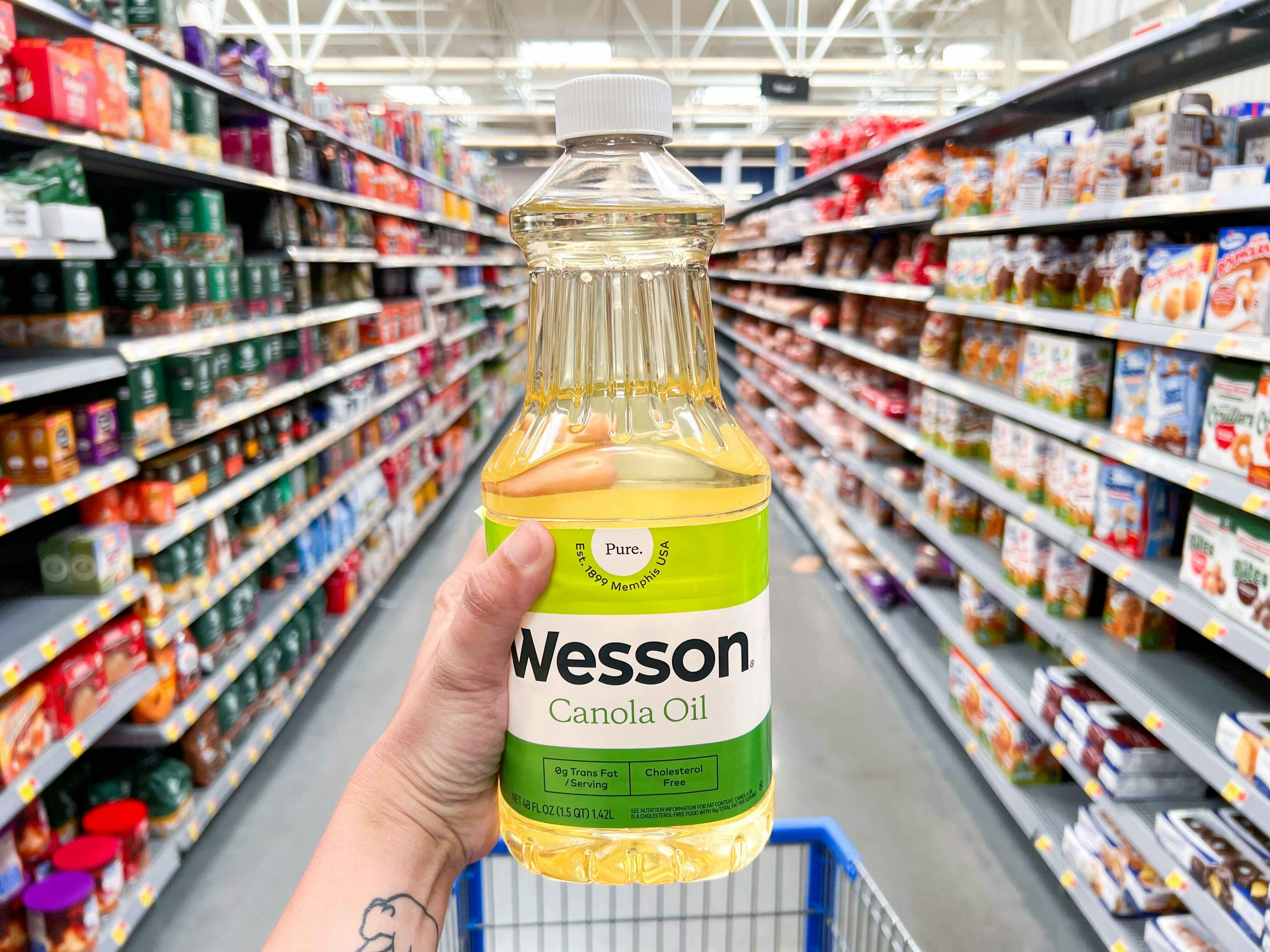 person holding wesson canola oil in walmart aisle 