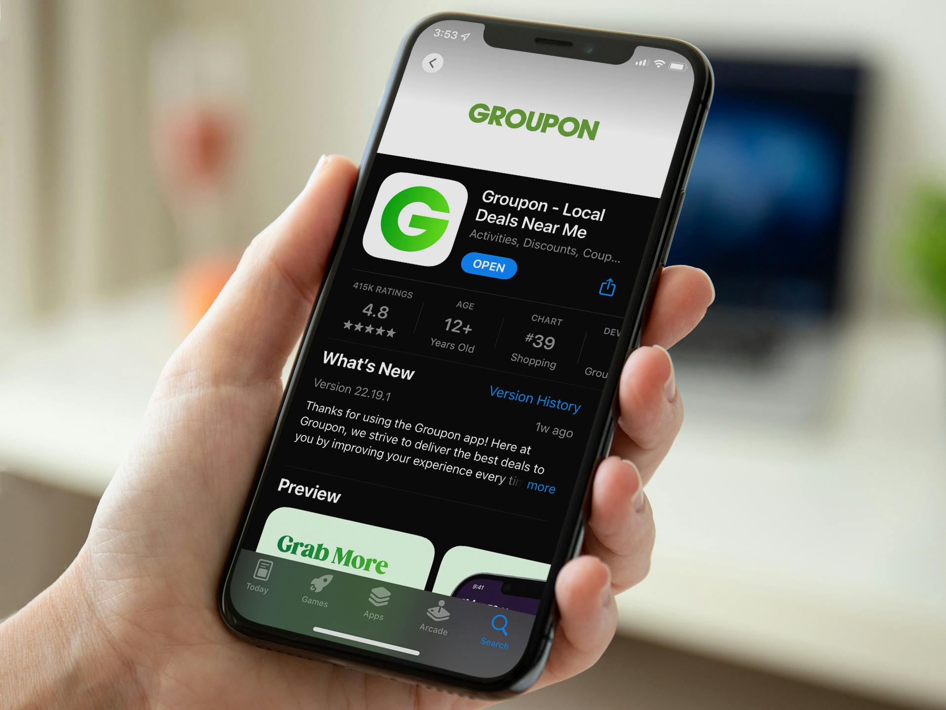 A person using a phone displaying the Groupon download page on the IOS app store.