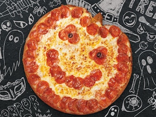 A pumpkin-shaped pizza from Papa John's set on a Halloween background