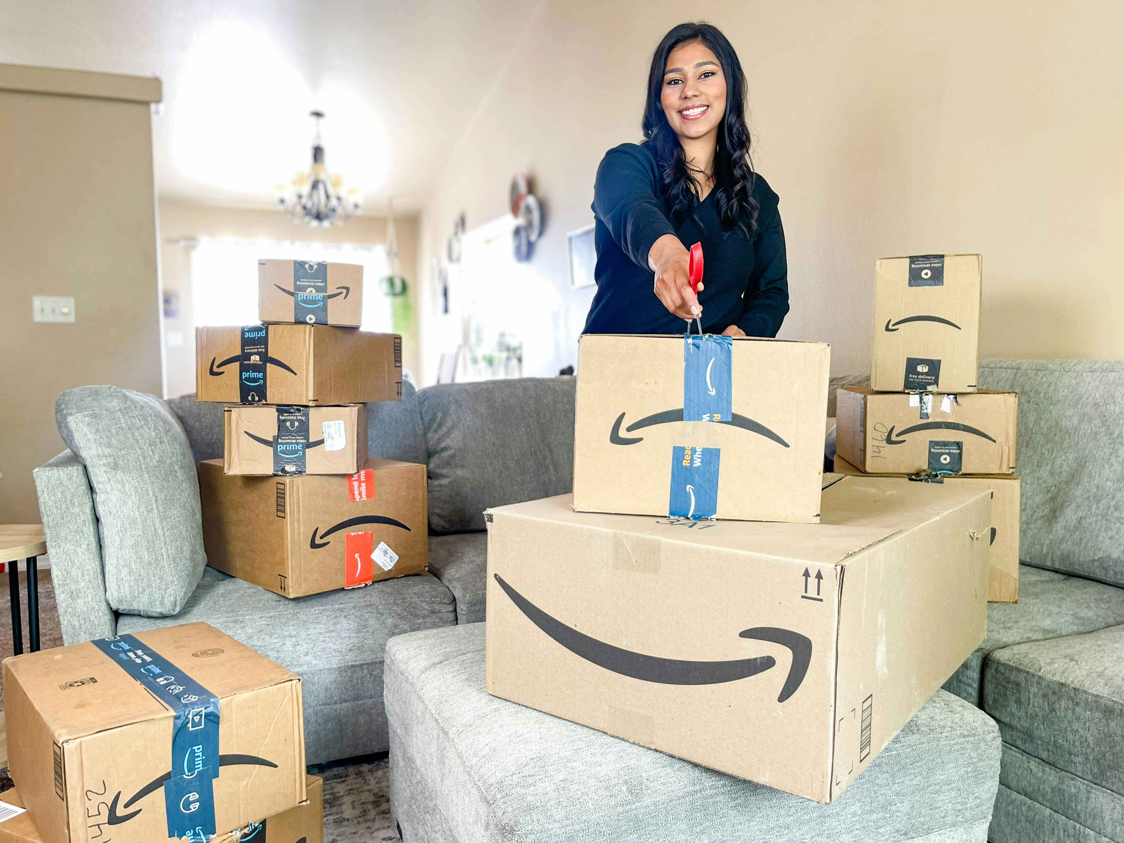 Person. opening an Amazon box. Surrounding them are stacks of differently size amazon boxes
