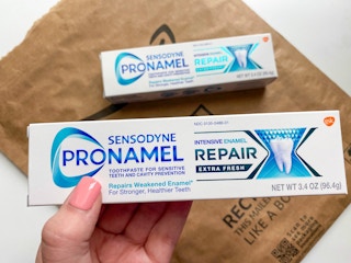 hand holding a tube of sensodyne toothpaste over an amazon package