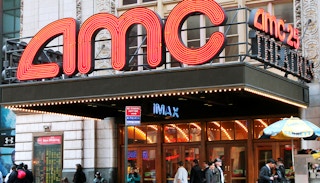 An AMC movie theater entrance with people walking by on the sidewalk