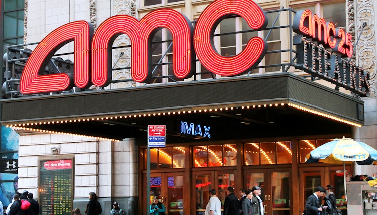 An AMC movie theater entrance with people walking by on the sidewalk