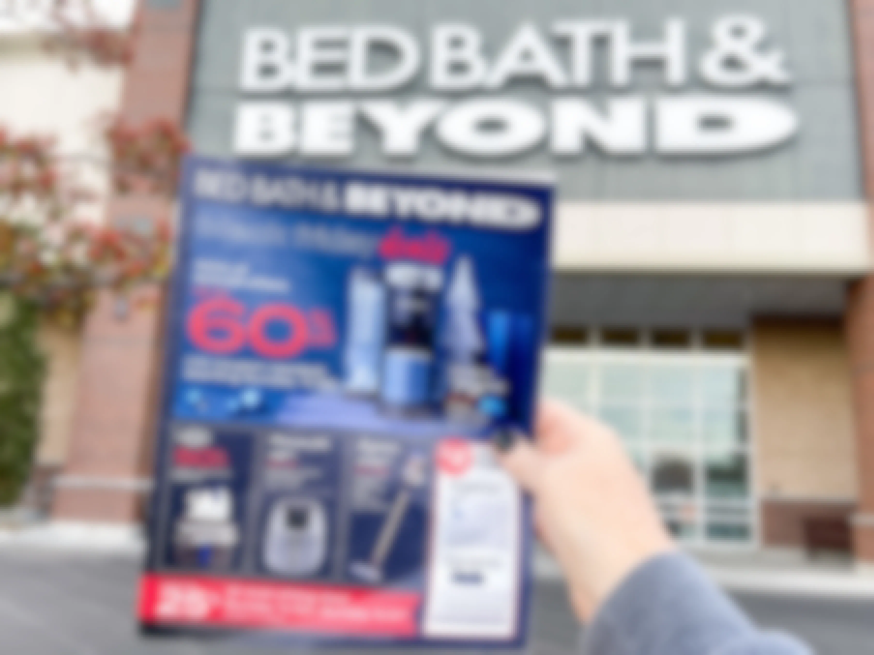 A person holding up the Bed Bath & Beyond Black Friday advertisement in front of a Bed Bath & Beyond store
