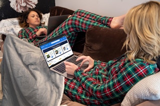 Two people sitting on a couch together, each looking at their laptops, one of their screens facing forward displaying the Walmart.com deals for laptops
