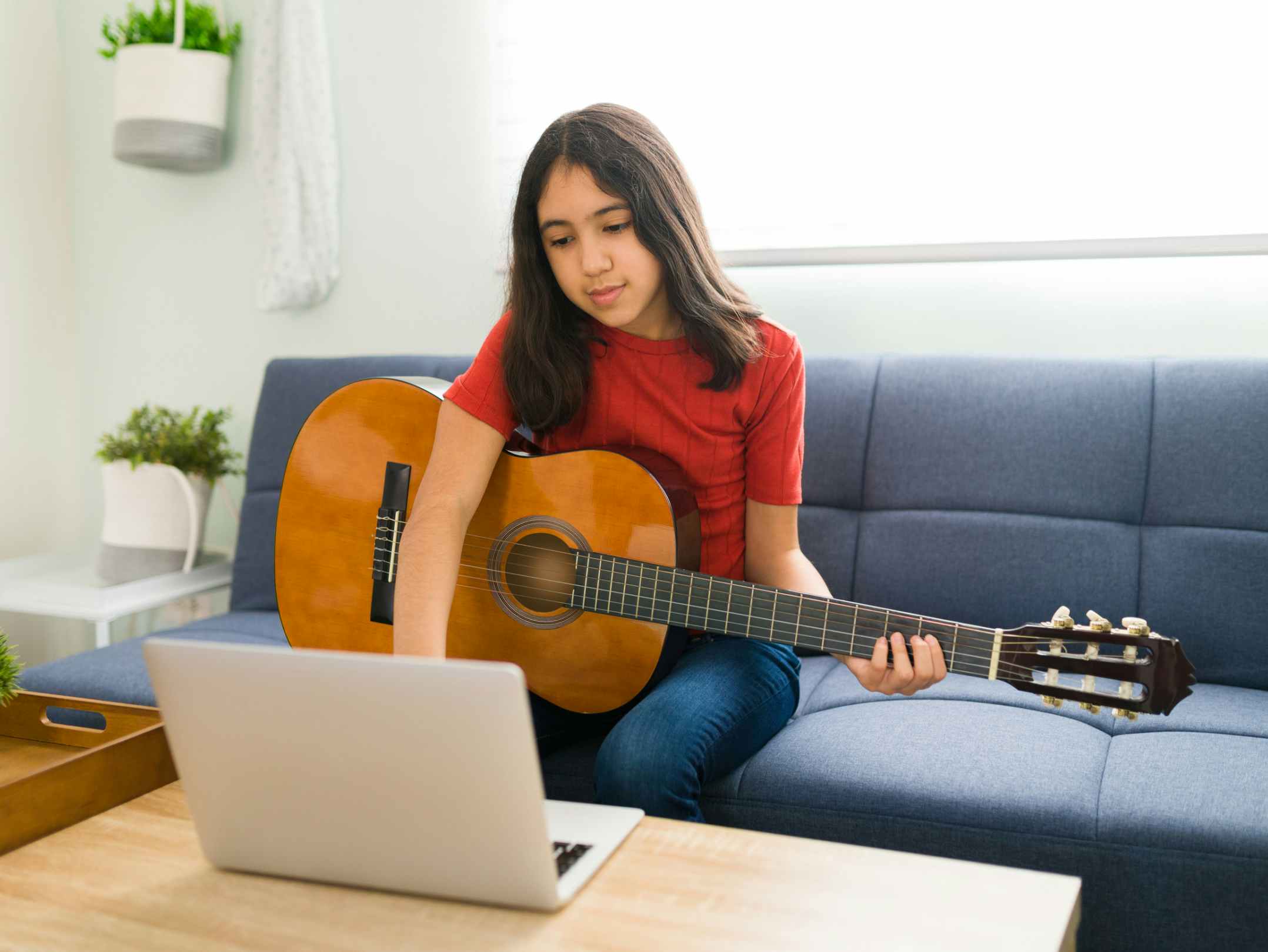 A teen playing guitar and looking at a laptop