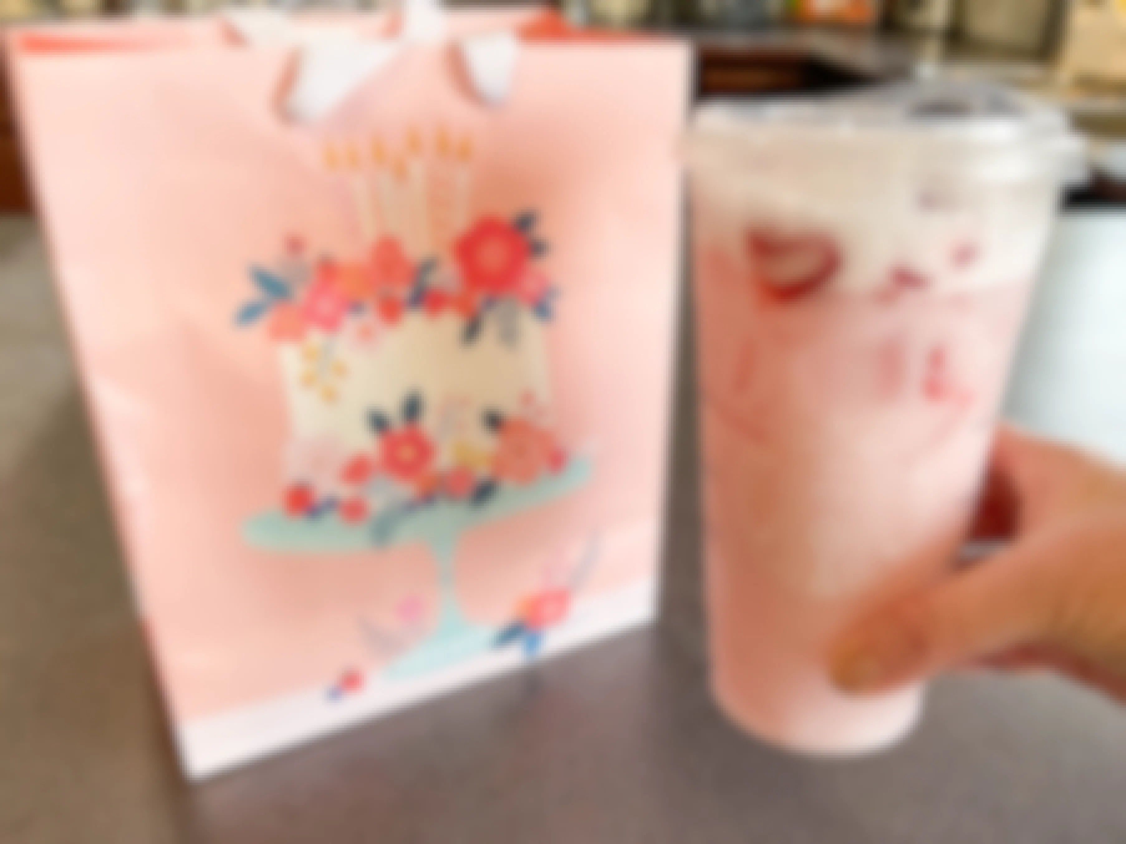 a starbucks pink drink next to a birthday gift bag 