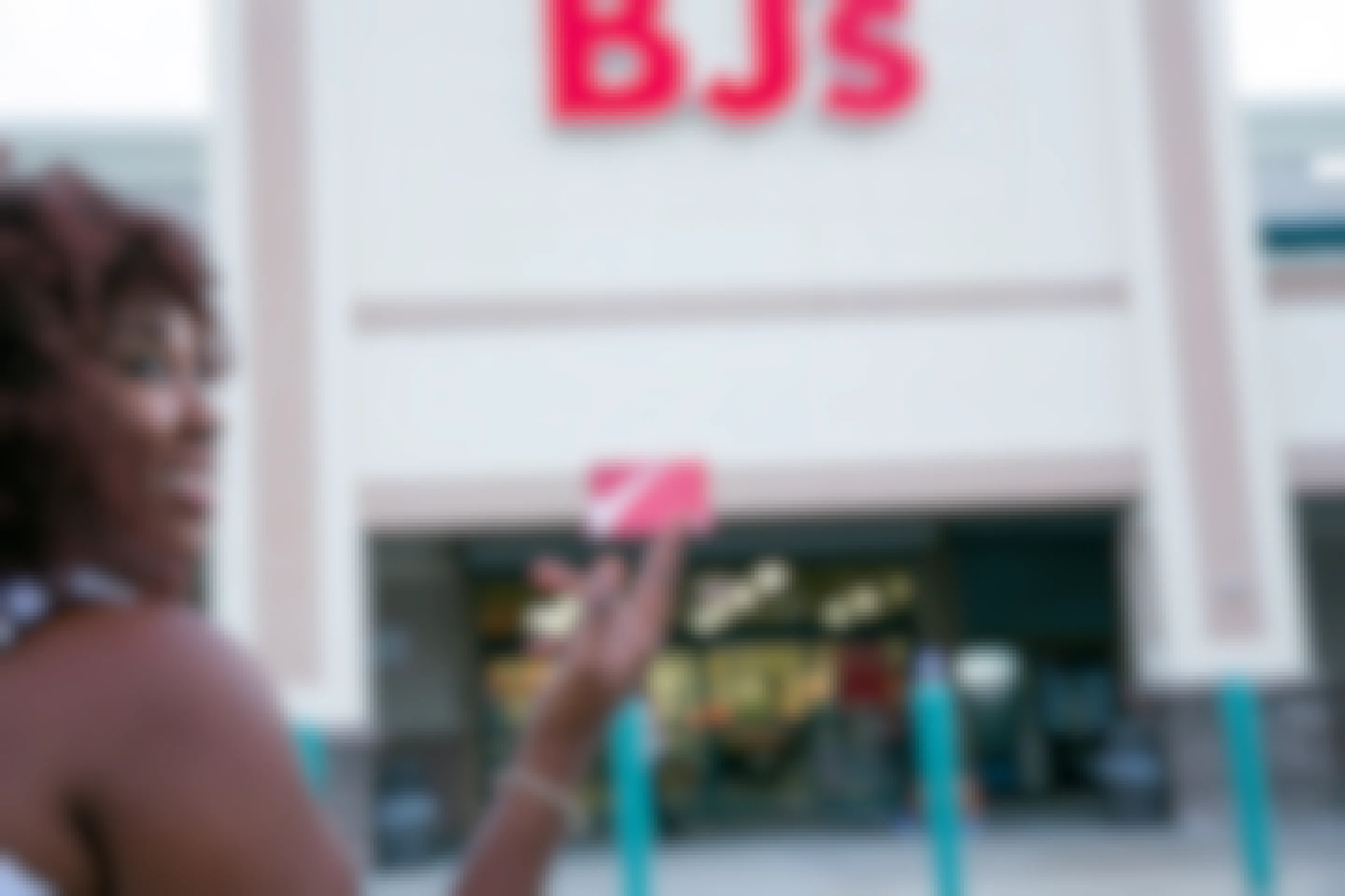 Person with curly hair holding a BJ's membership card infront of the BJ's store