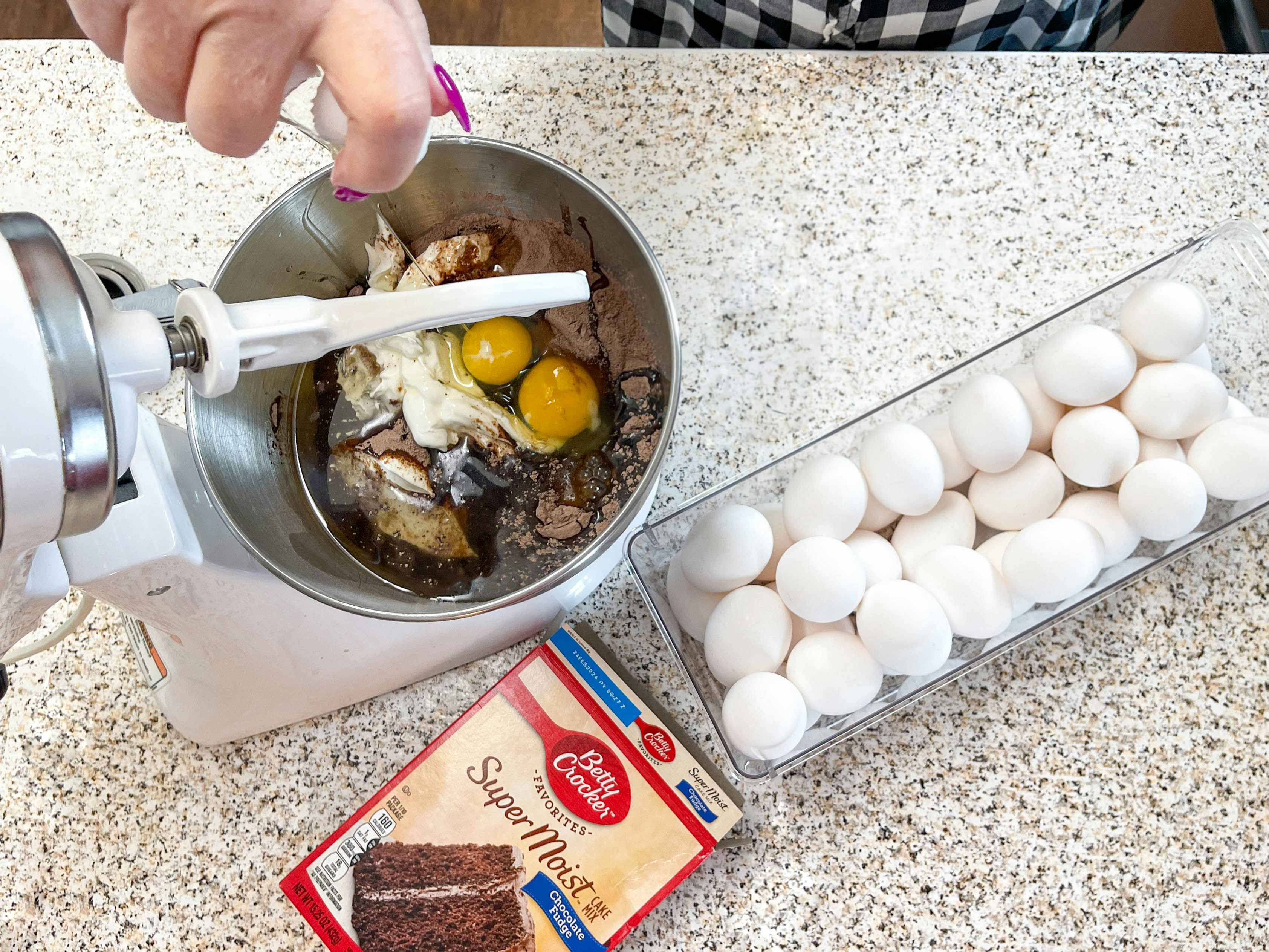 a person adding eggs into a mixer to make a boxed cake 