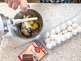 a person adding eggs into a mixer to make a boxed cake