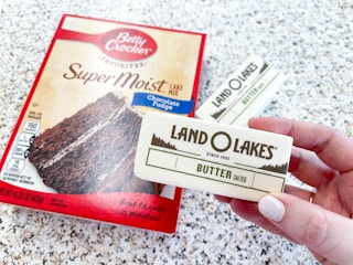 a person holding butter next to a box of cake mix