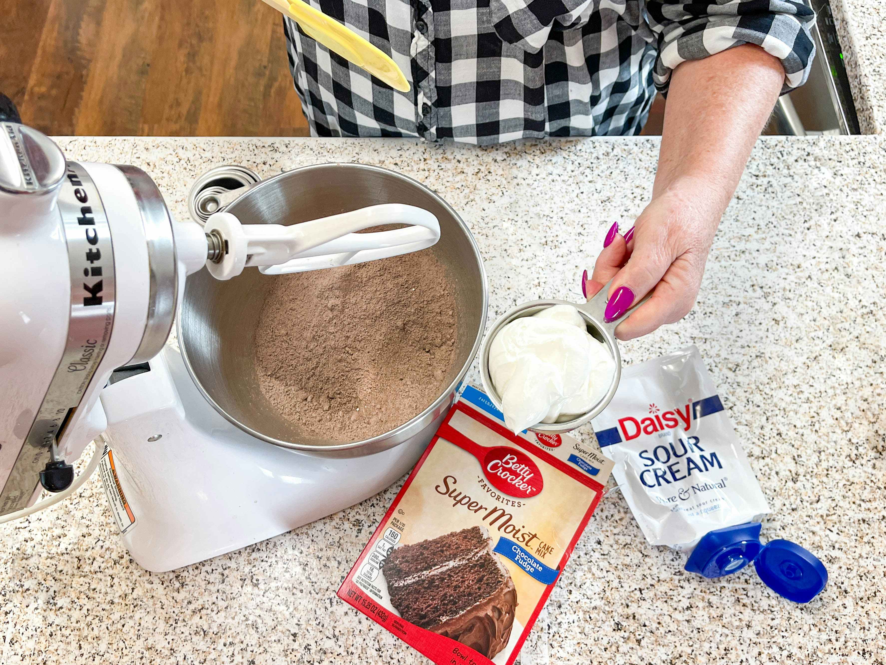 a person about to add sour cream into a mixer with boxed cake mix inside 